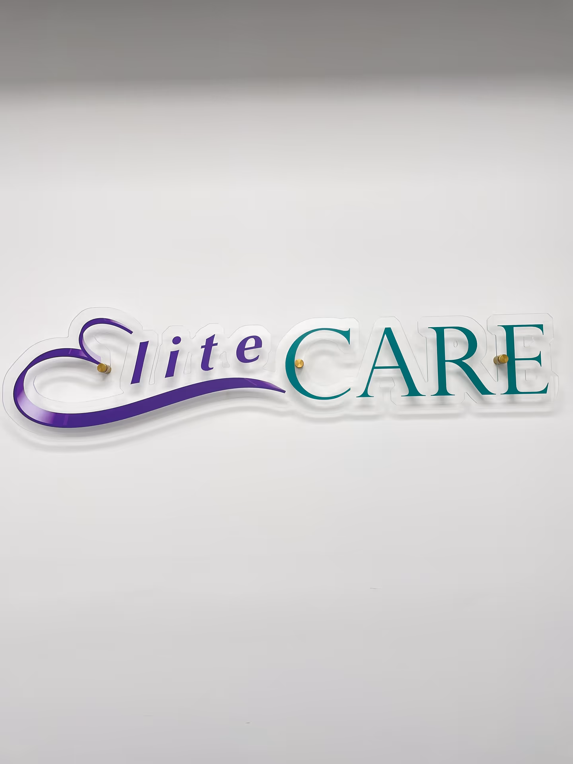 White wall with a purple and teal Elite CARE sign mounted on it.