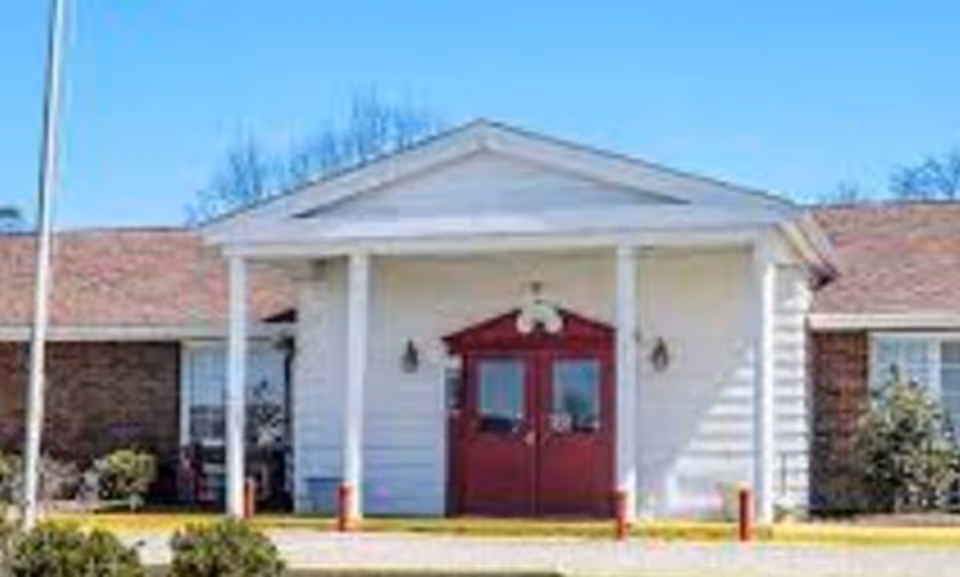 Front entrance of a single-story building with white siding and red double doors.
