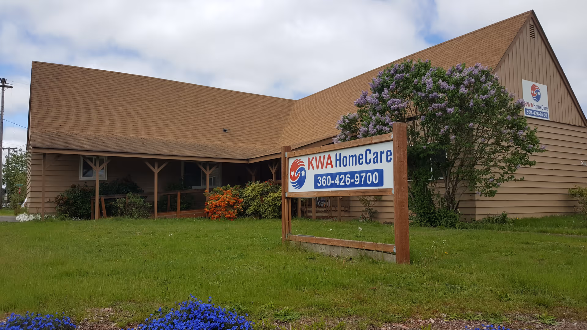 A single-story brown building with a KWA HomeCare sign and flowering tree.