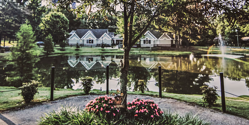 Exterior view of Foxbridge senior living with pond, fountain, and landscaped foreground.