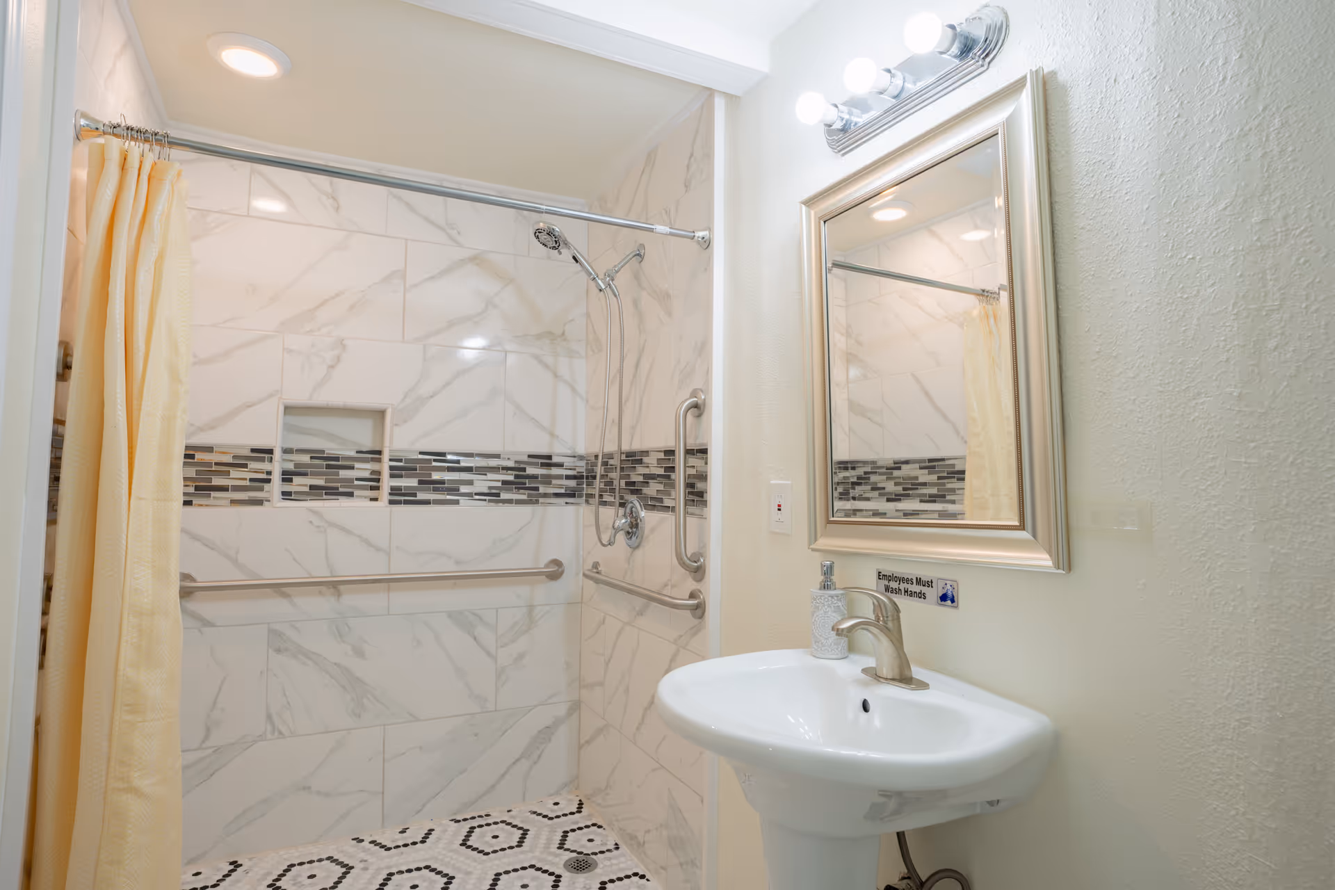 Accessible bathroom featuring tiled shower with grab bars, recessed niche, shower curtain, sink, and mirror.