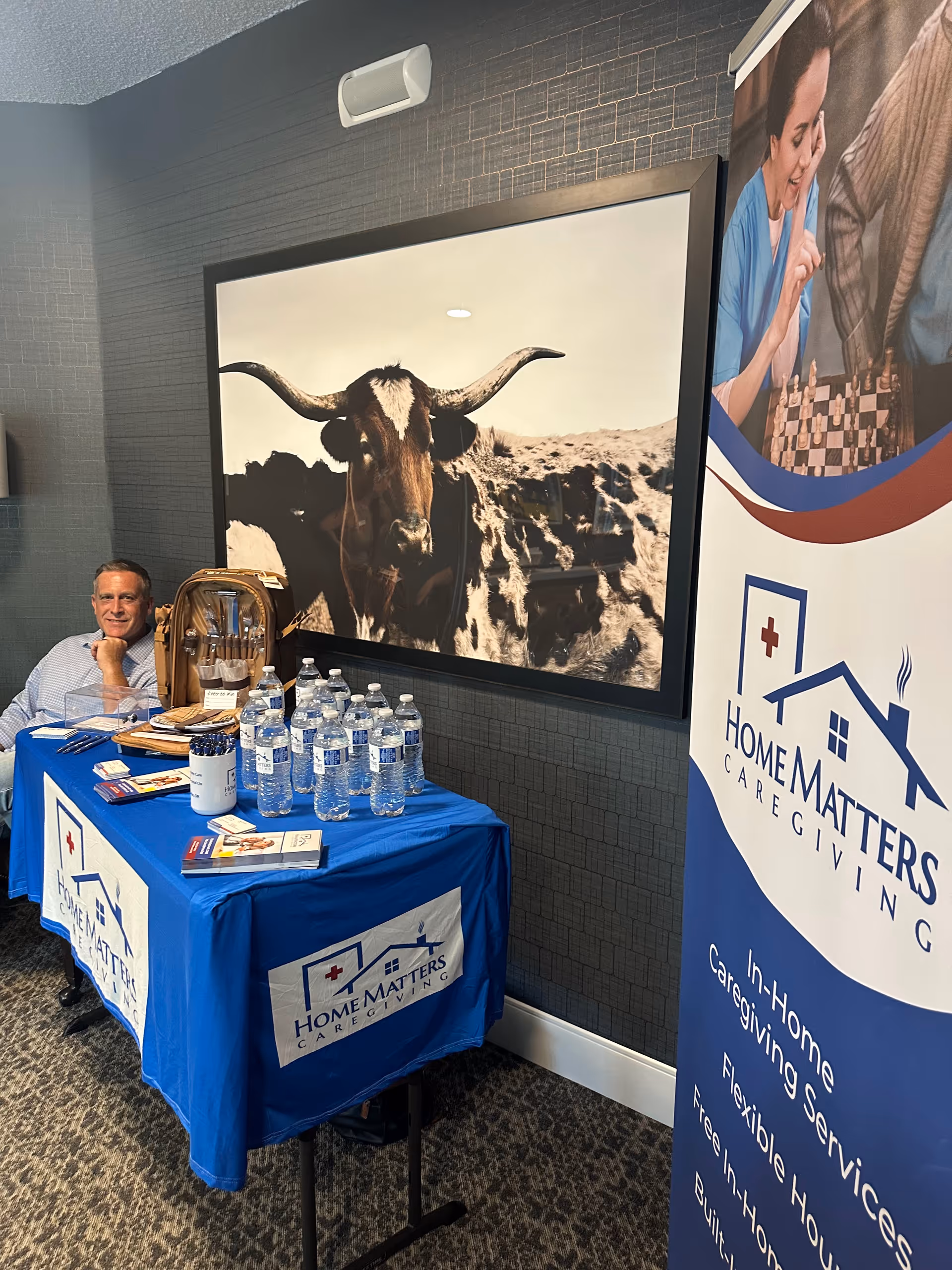 Man sits at a blue-clothed promotional table with water bottles beside a Home Matters banner