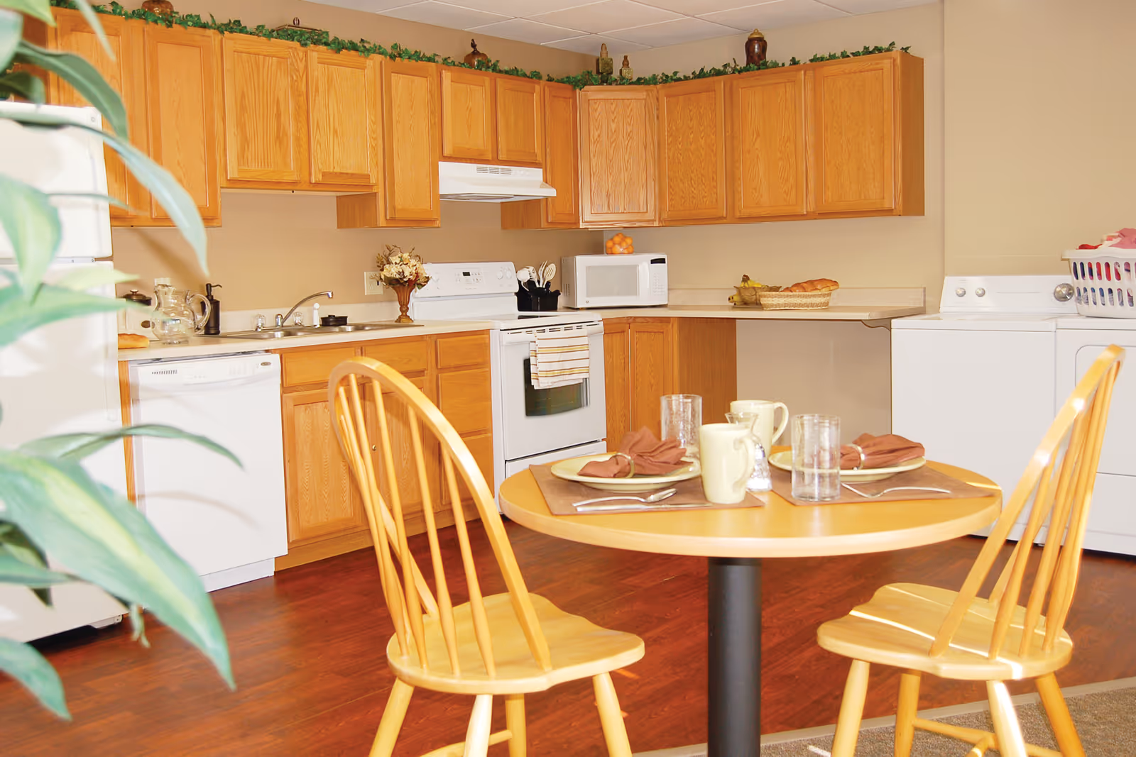 Bright kitchen area with wooden cabinets, appliances, and a small round dining table set for two.