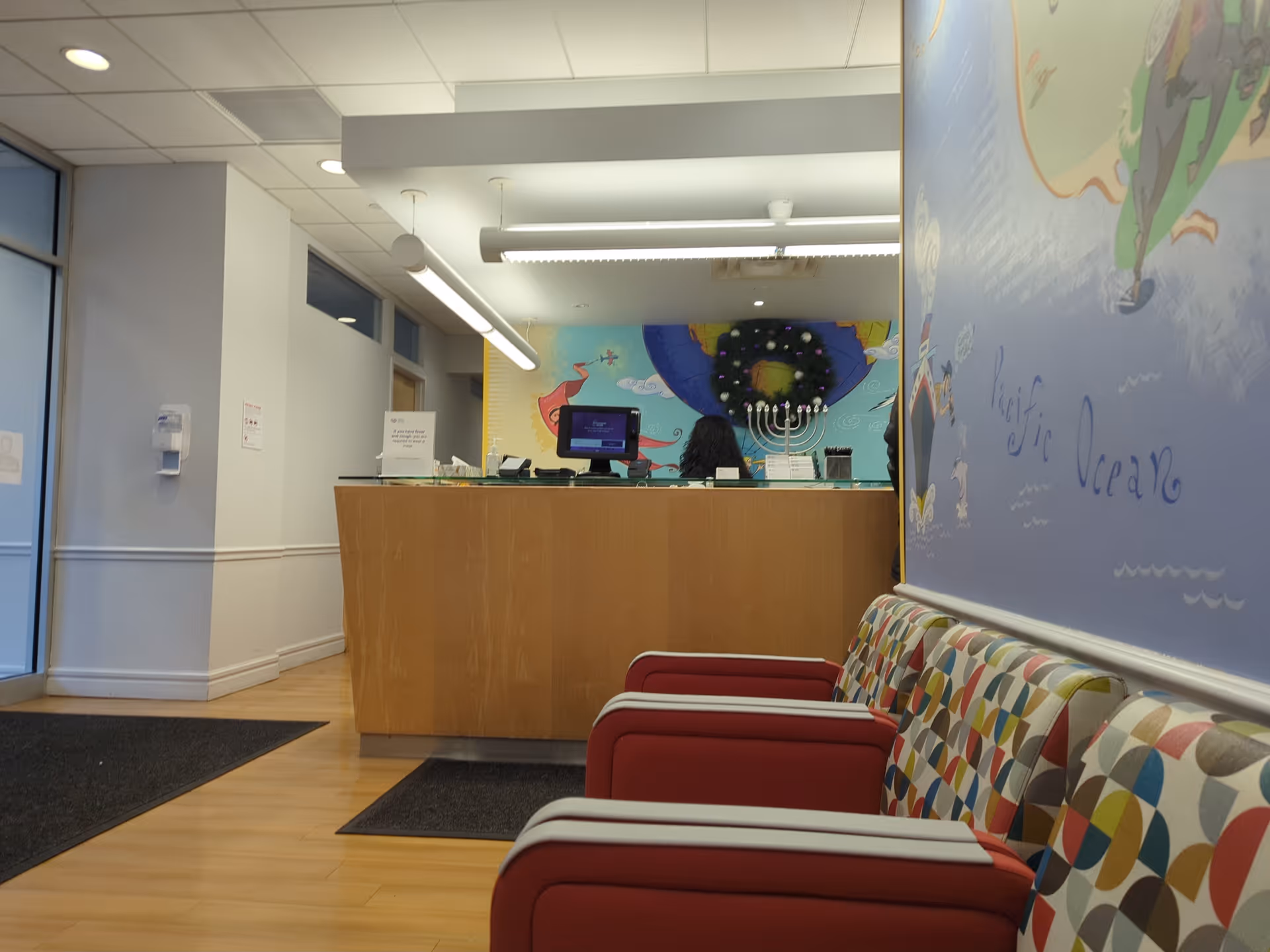 Interior reception area with a wooden front desk, mural, and colorful seating along the wall.