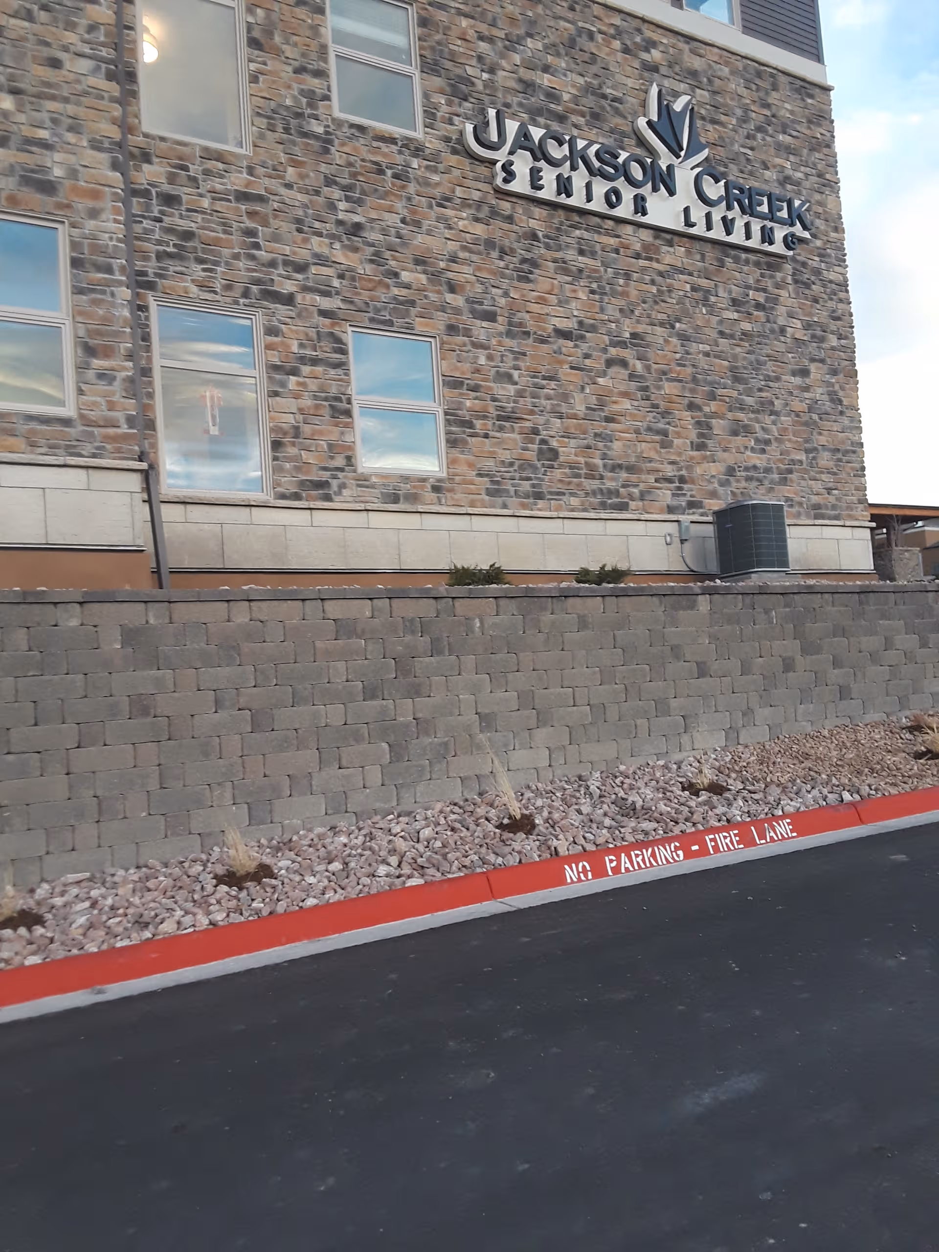 Exterior view of Jackson Creek Senior Living building with stone facade and red fire-lane curb.