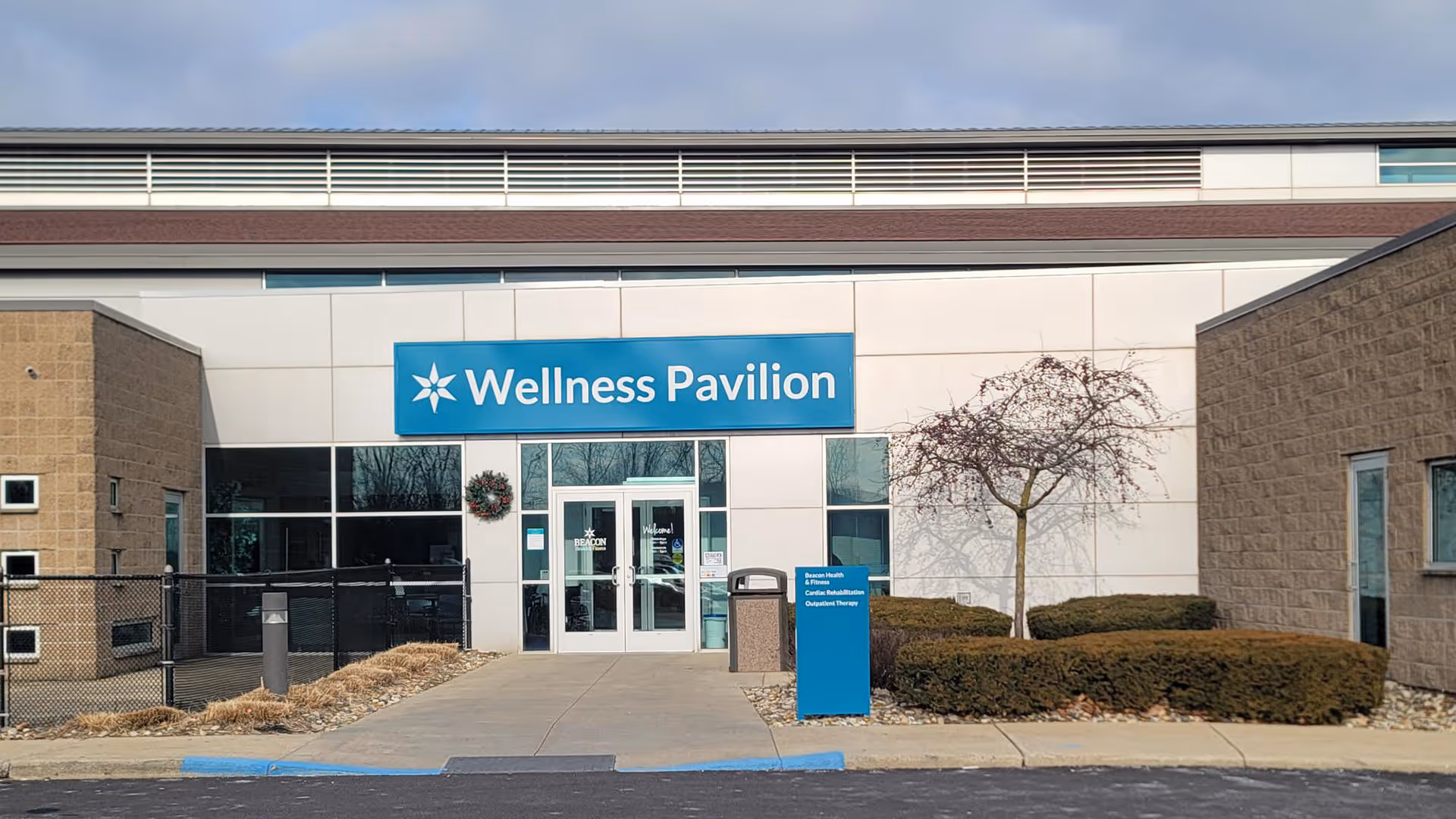 Exterior view of a facility entrance with a blue Wellness Pavilion sign above doors.