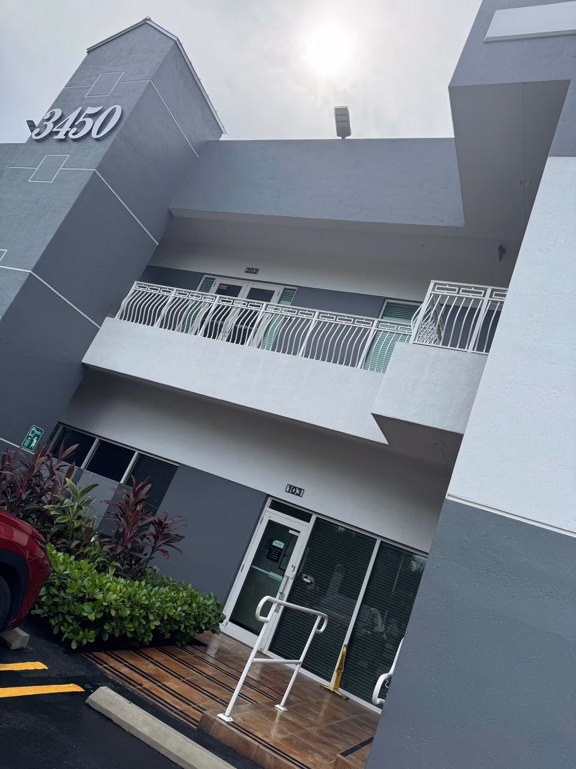 Front exterior of a modern gray building with entrance, balconies, and decorative railings.