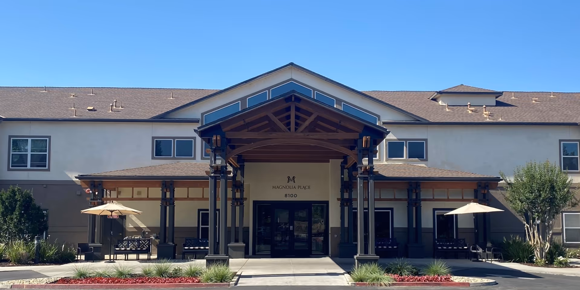 Front exterior view of Magnolia Place senior living facility with a covered entrance and patio seating.