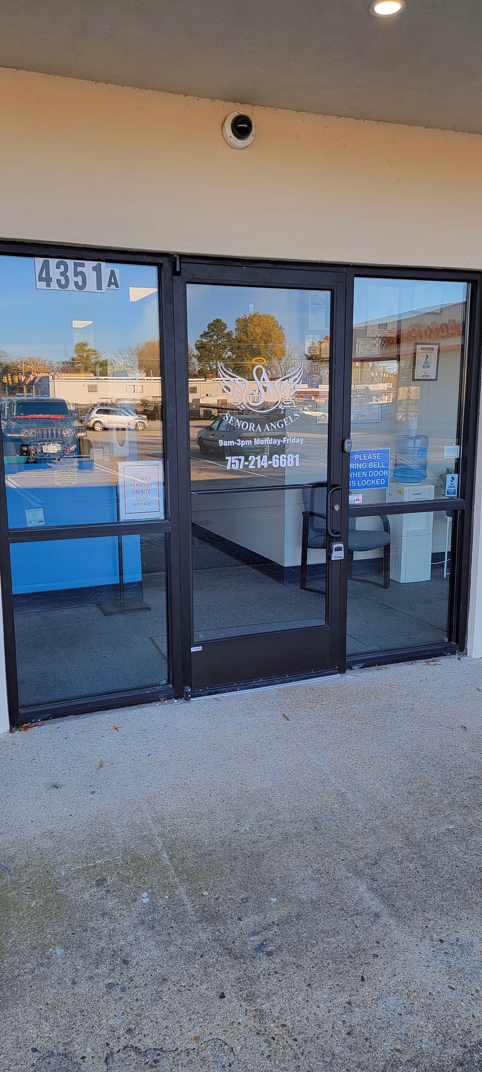 Glass front doors with a logo and reflection of parked cars outside.