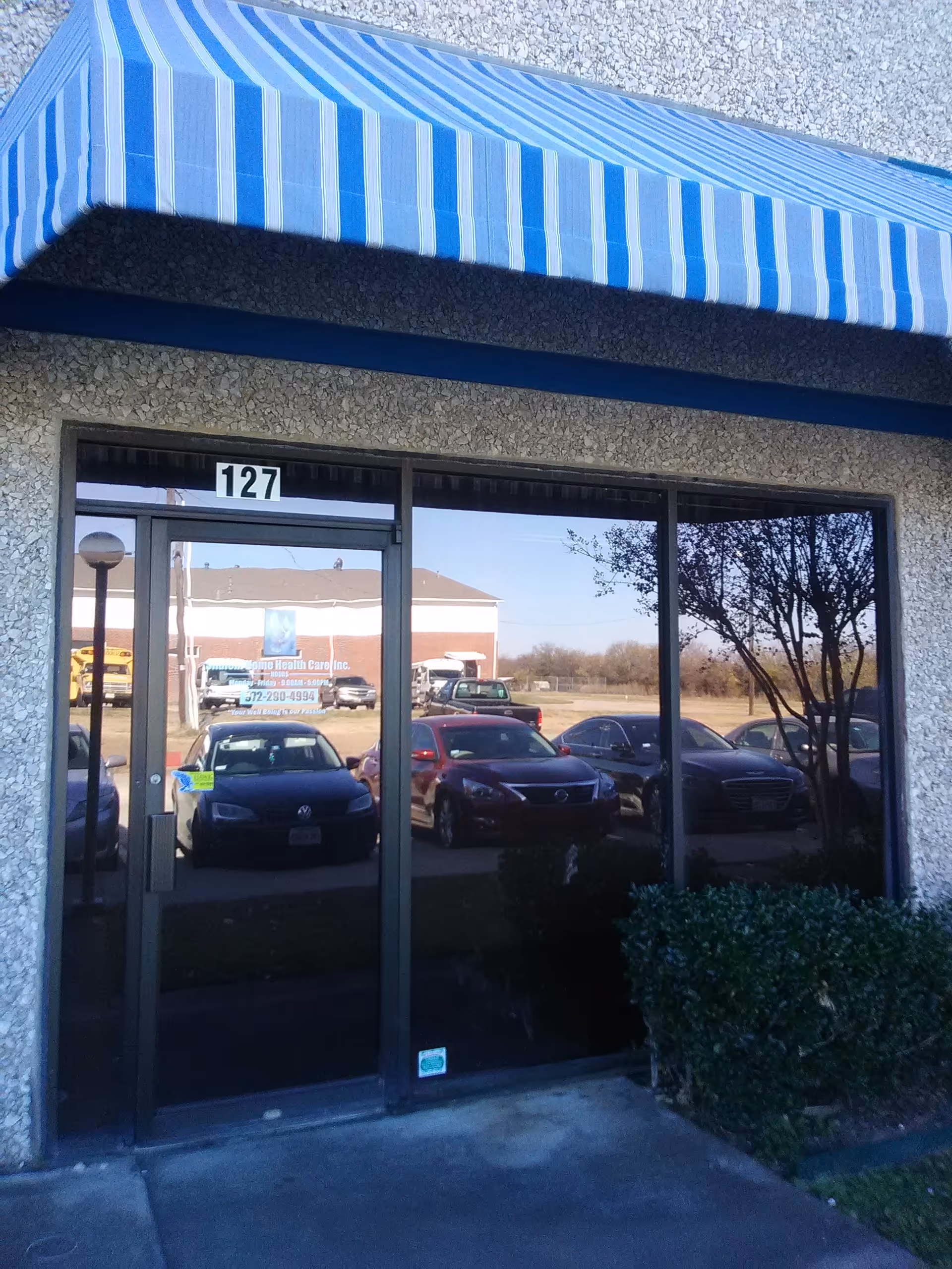 Front entrance with striped blue awning and cars reflected in glass doors.
