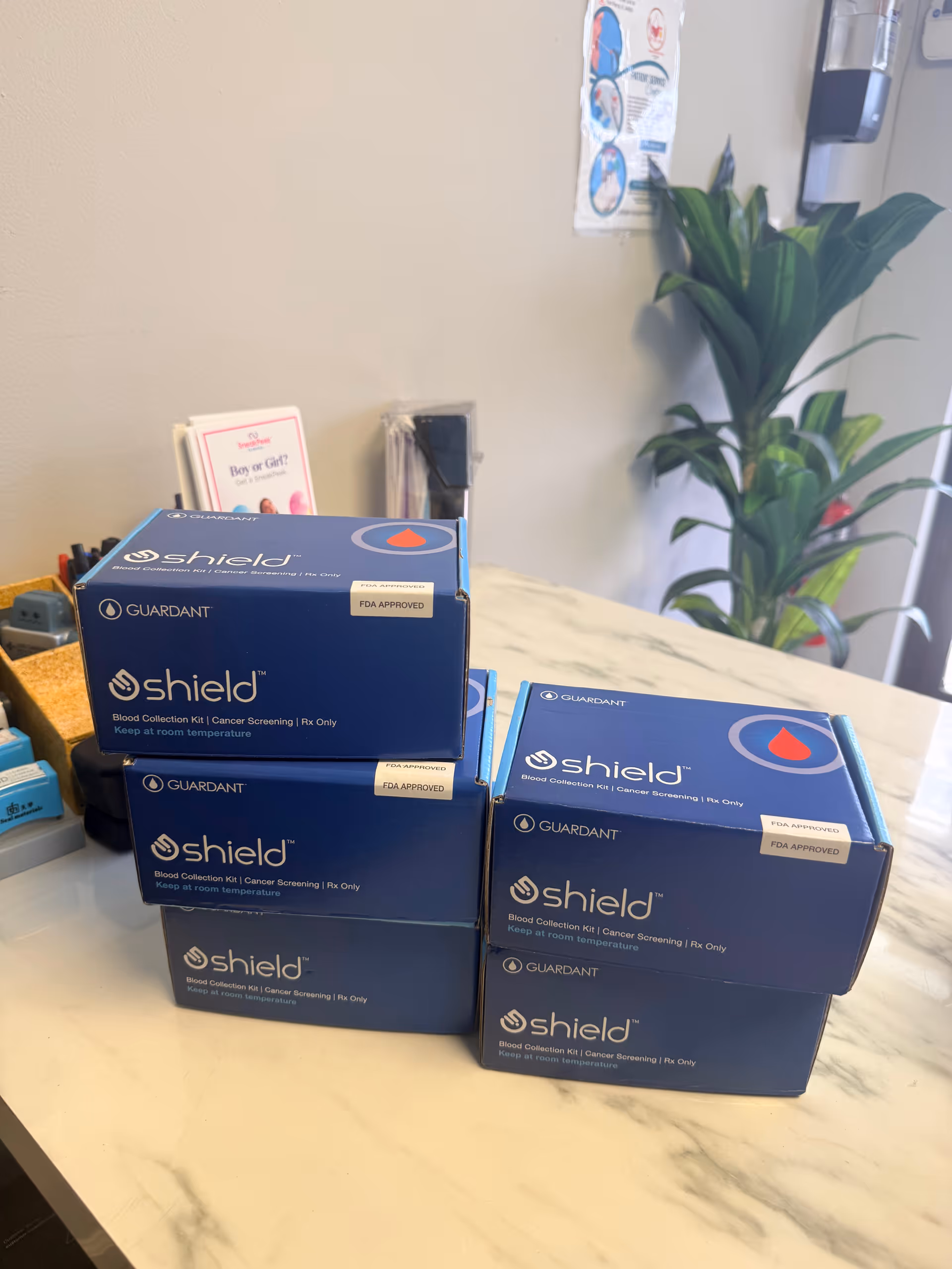 Stacked blue Shield blood collection kit boxes on a white marble clinic counter