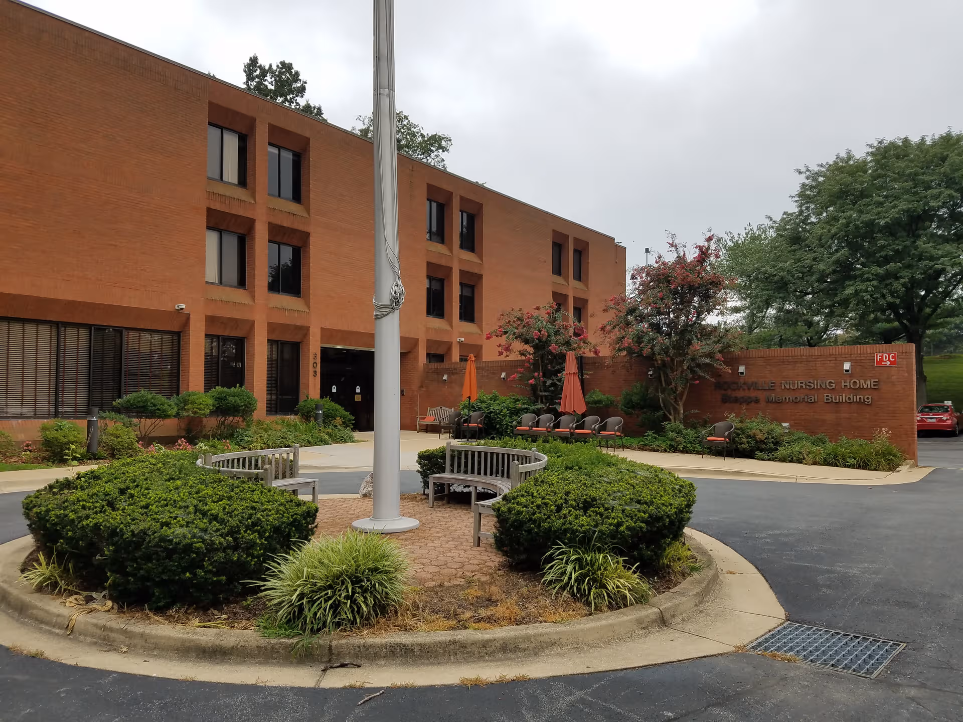 Brick nursing home exterior with circular driveway and benches in a landscaped front plaza