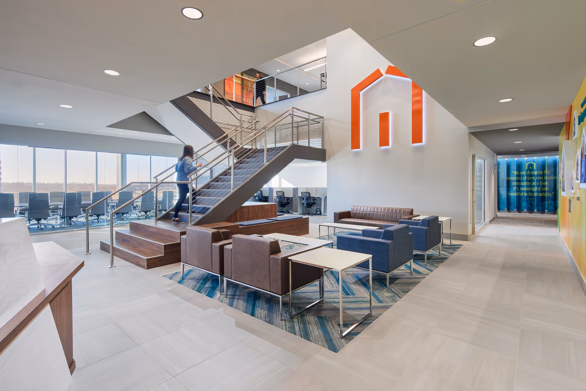 Bright corporate lobby with seating, a glass staircase, and a large wall logo.