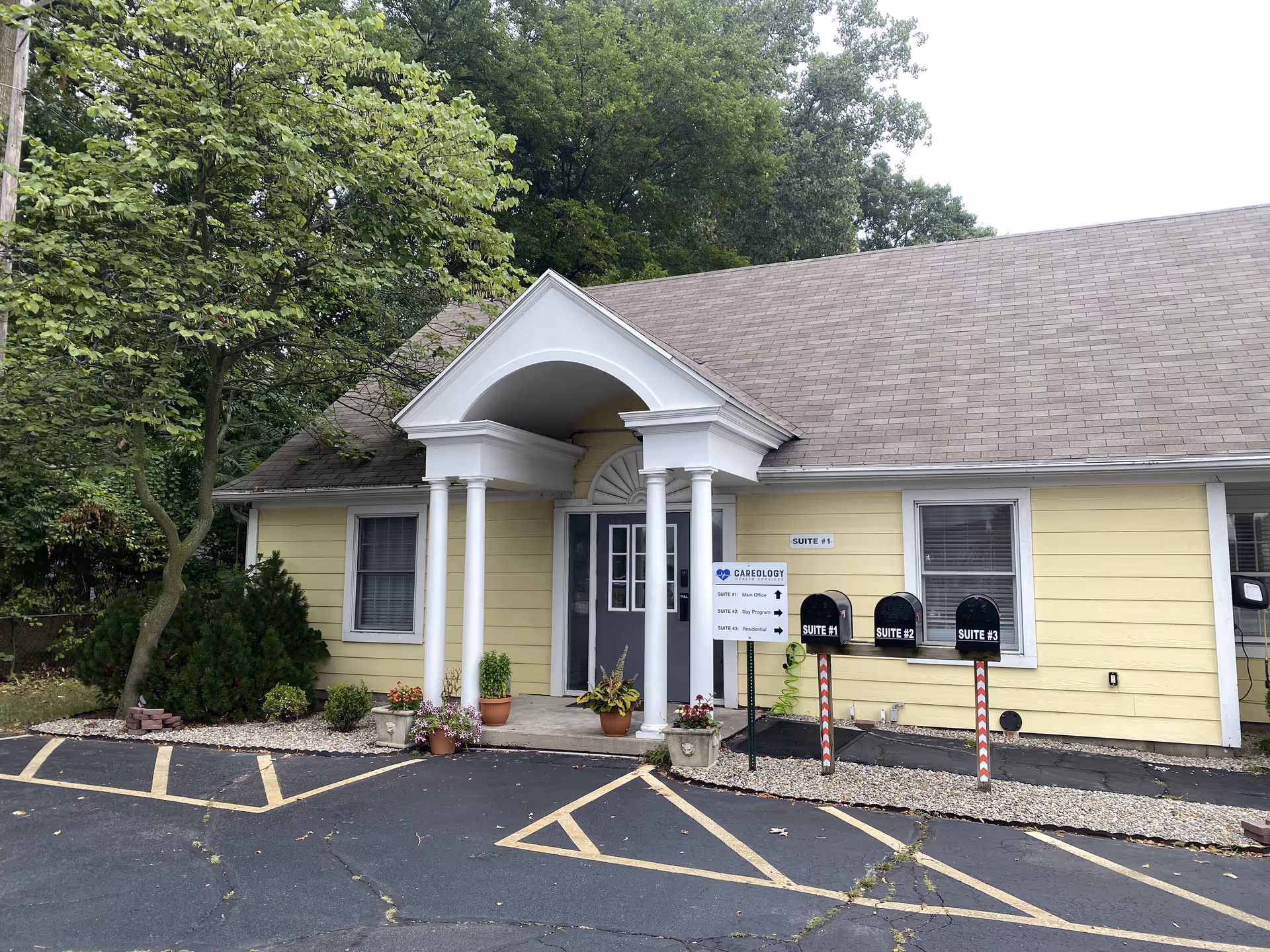 Small yellow building with white columns, portico, front entrance, and parking lot.