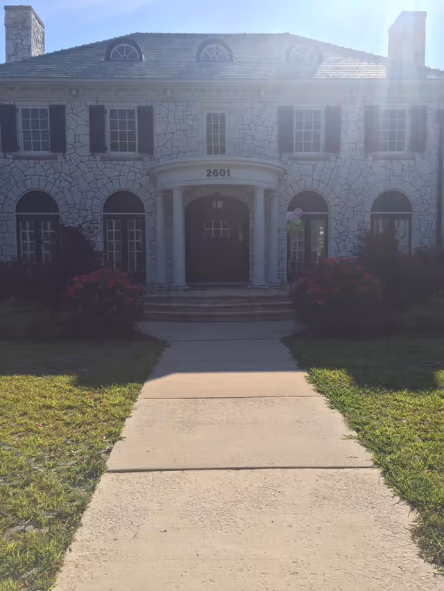 Stone-front senior living facility with arched windows and a central entrance along a walkway.