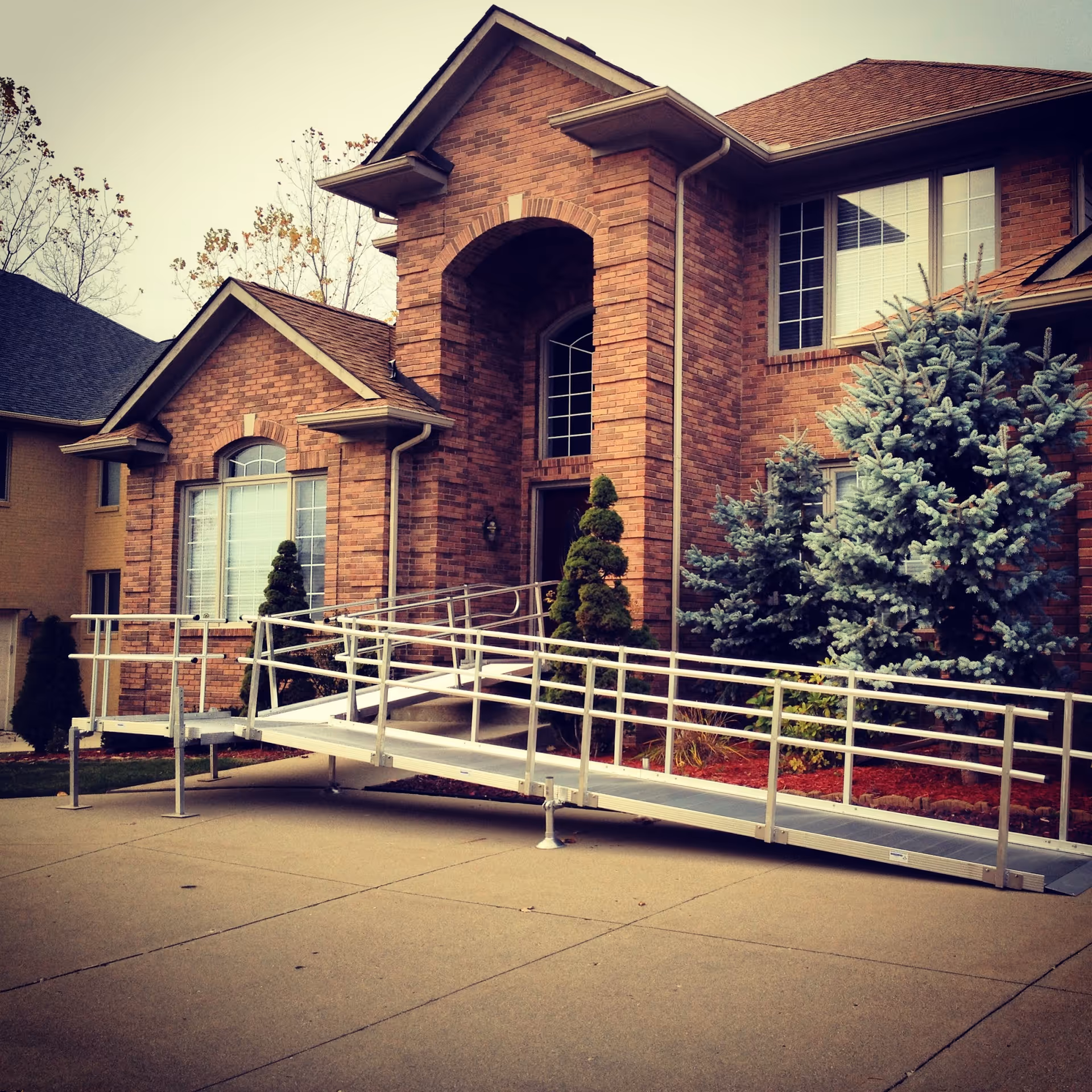 Brick senior living facility with a metal wheelchair ramp leading to the front entrance.