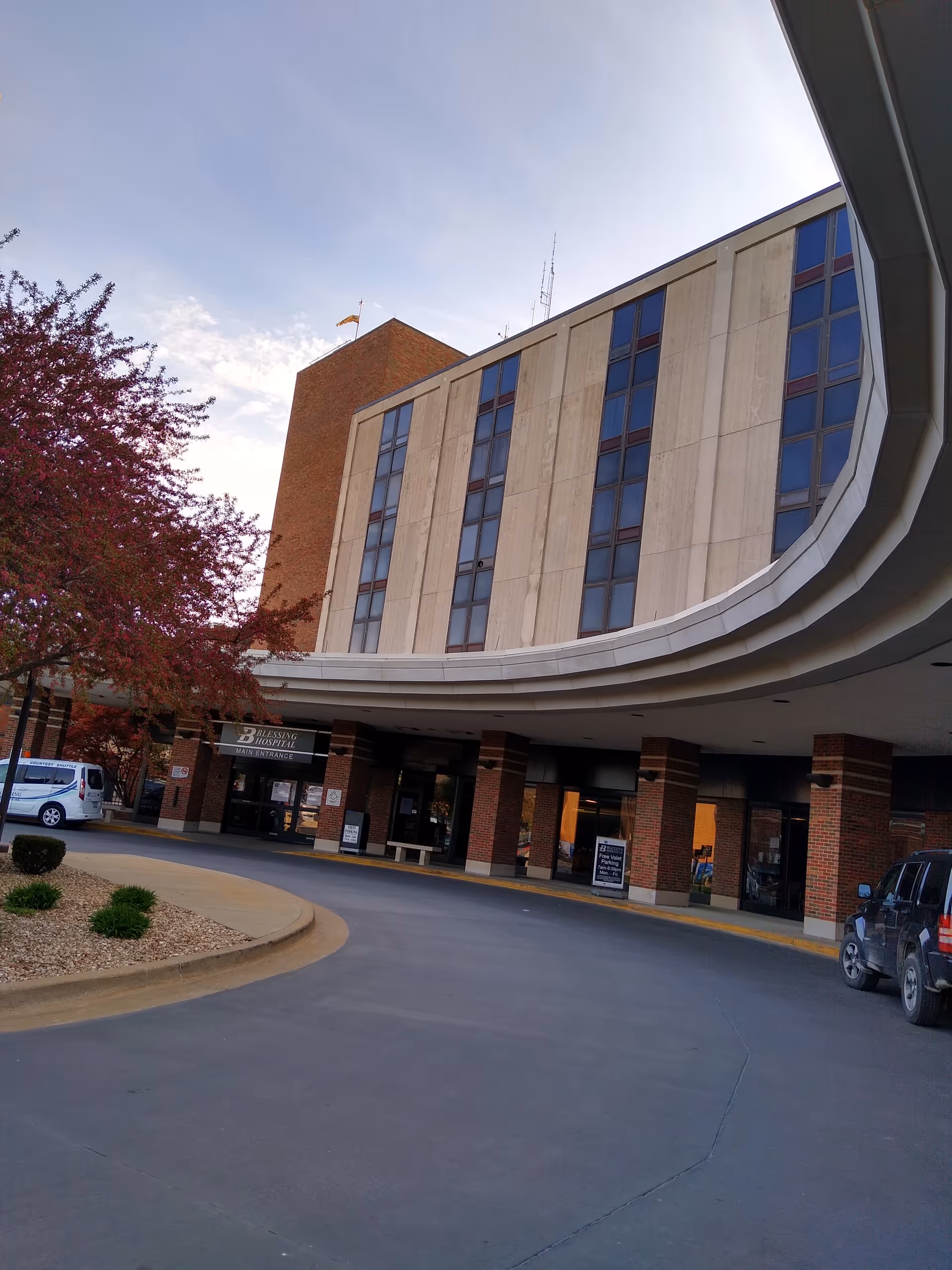 Curved entrance of Blessing Hospital with brick columns and glass windows.