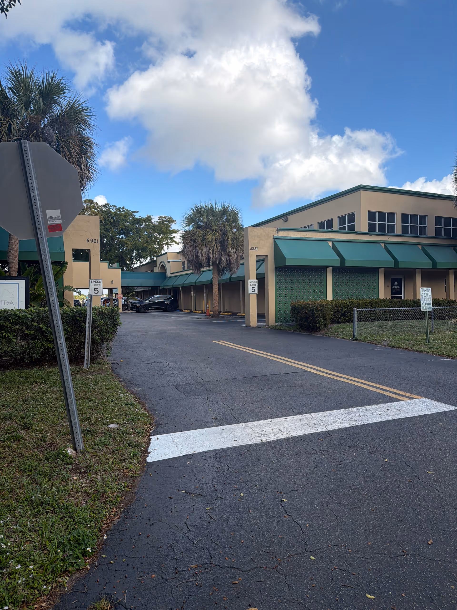 Exterior view of a senior living facility with green awnings and palm trees along a driveway