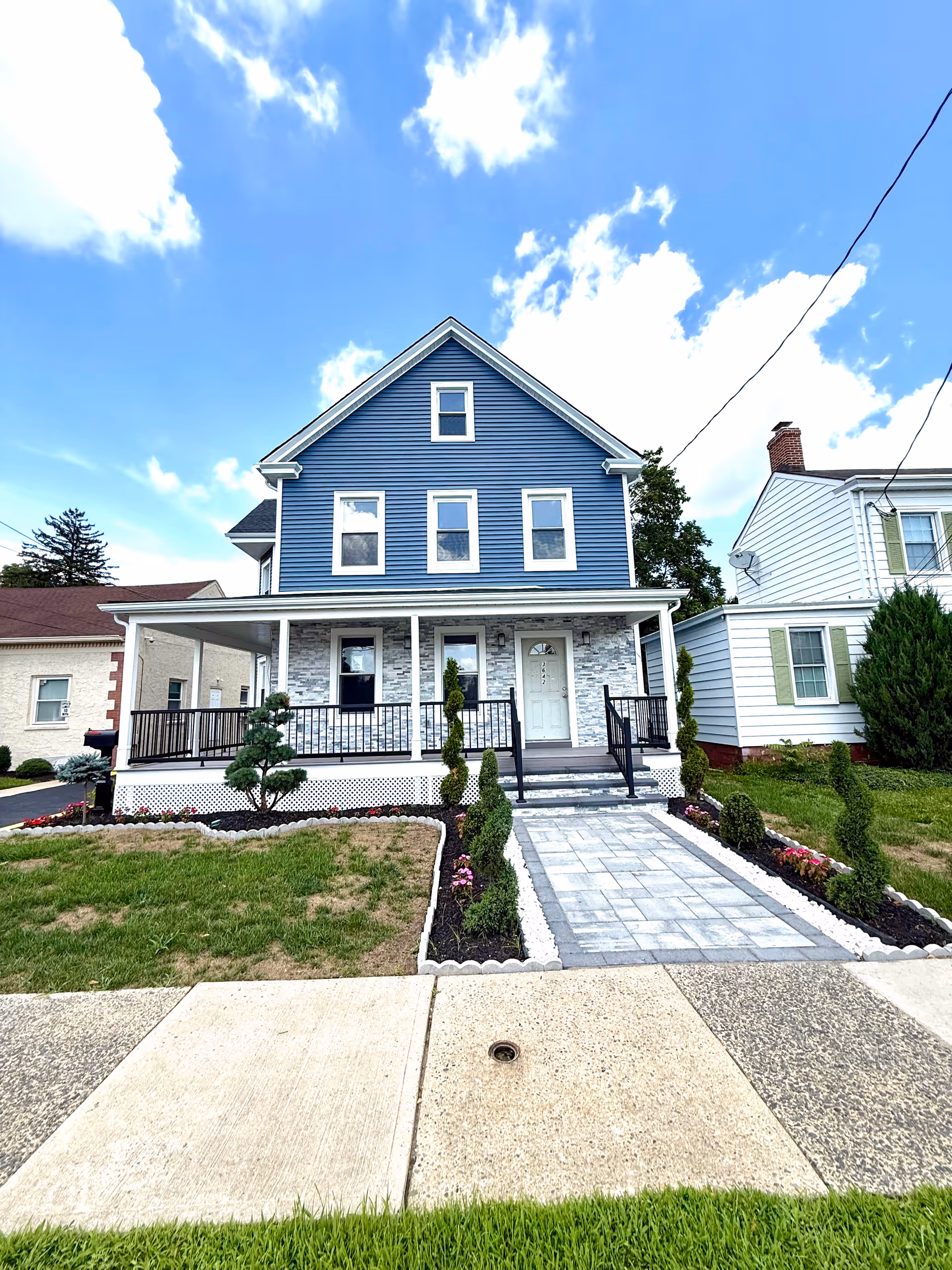 Blue two-story house with a front porch, walkway, and manicured lawn.