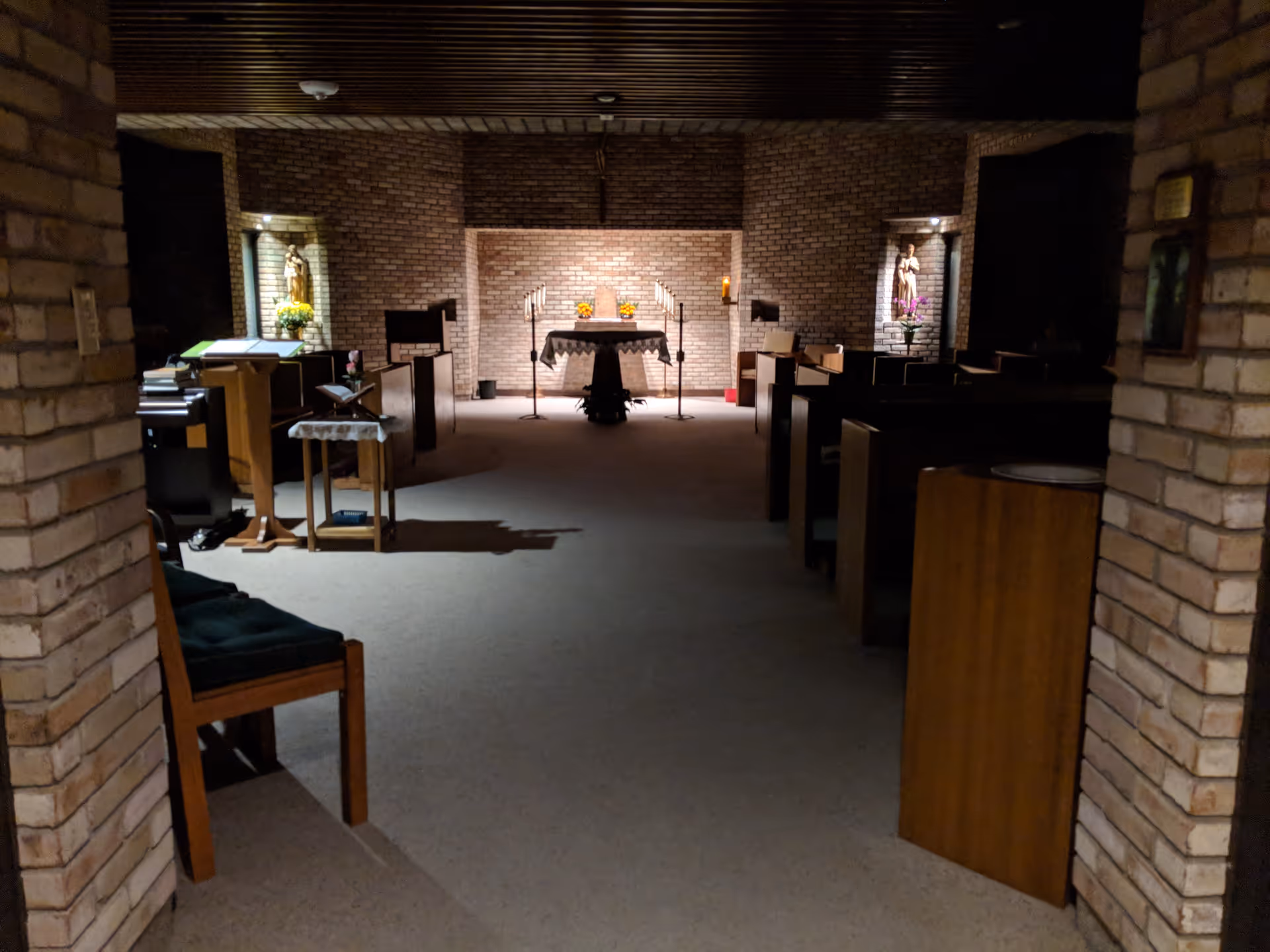 A dim chapel interior with brick walls, an altar, statues, and pews.
