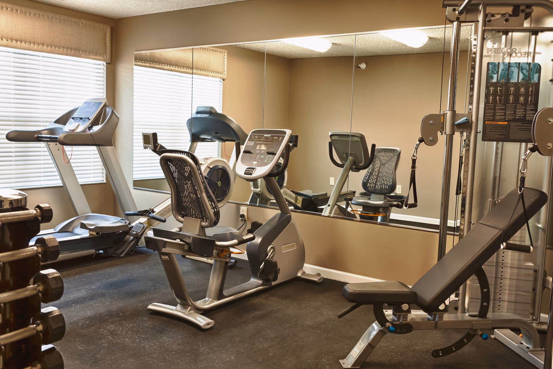 Indoor senior living fitness center with treadmills, stationary bike, and weight machines.