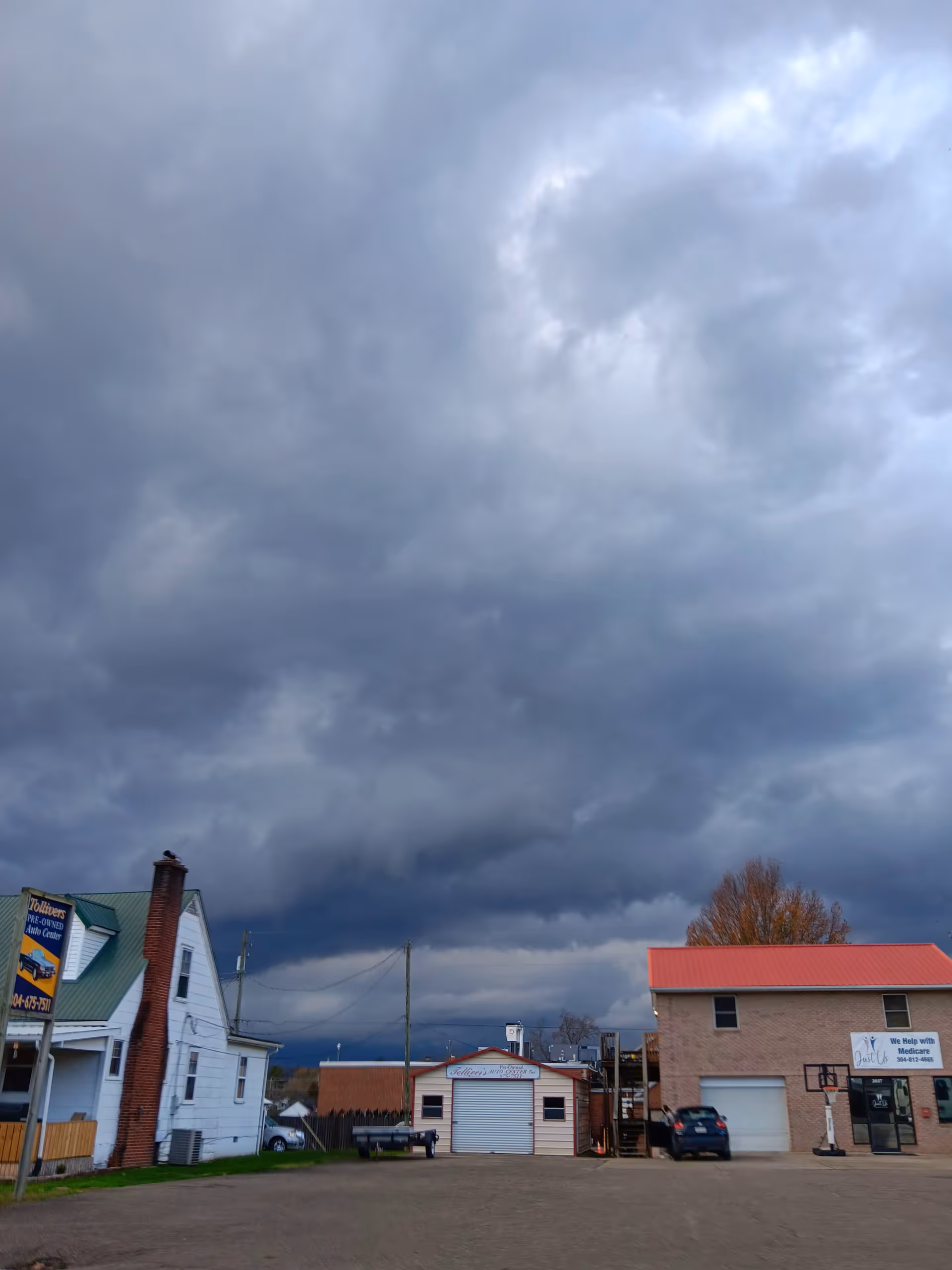 Cloudy, dark storm clouds loom over a small town street with storefronts and parked cars.