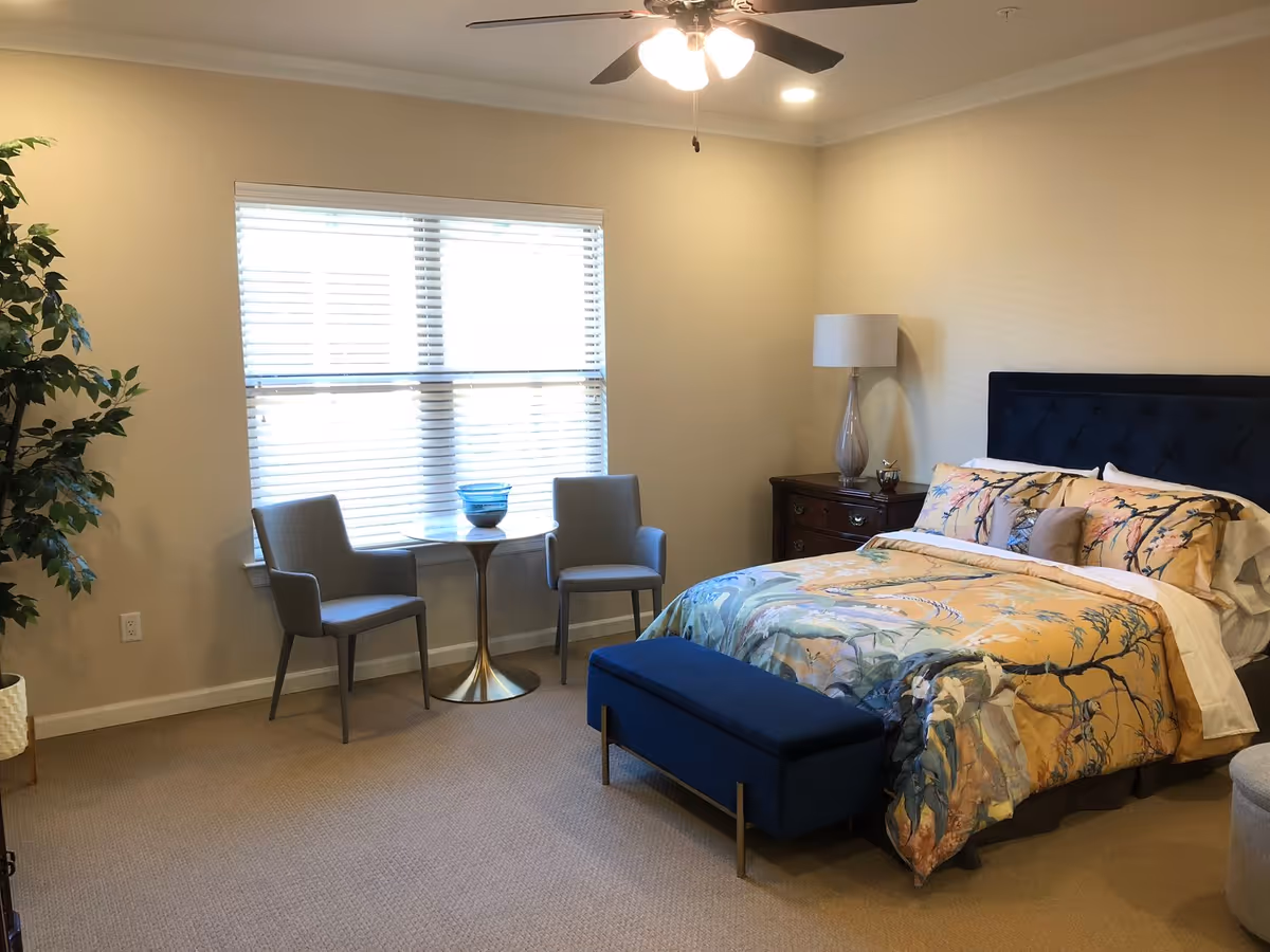 Bright bedroom in Windhaven Senior Living with a bed, window seating, and a nightstand.