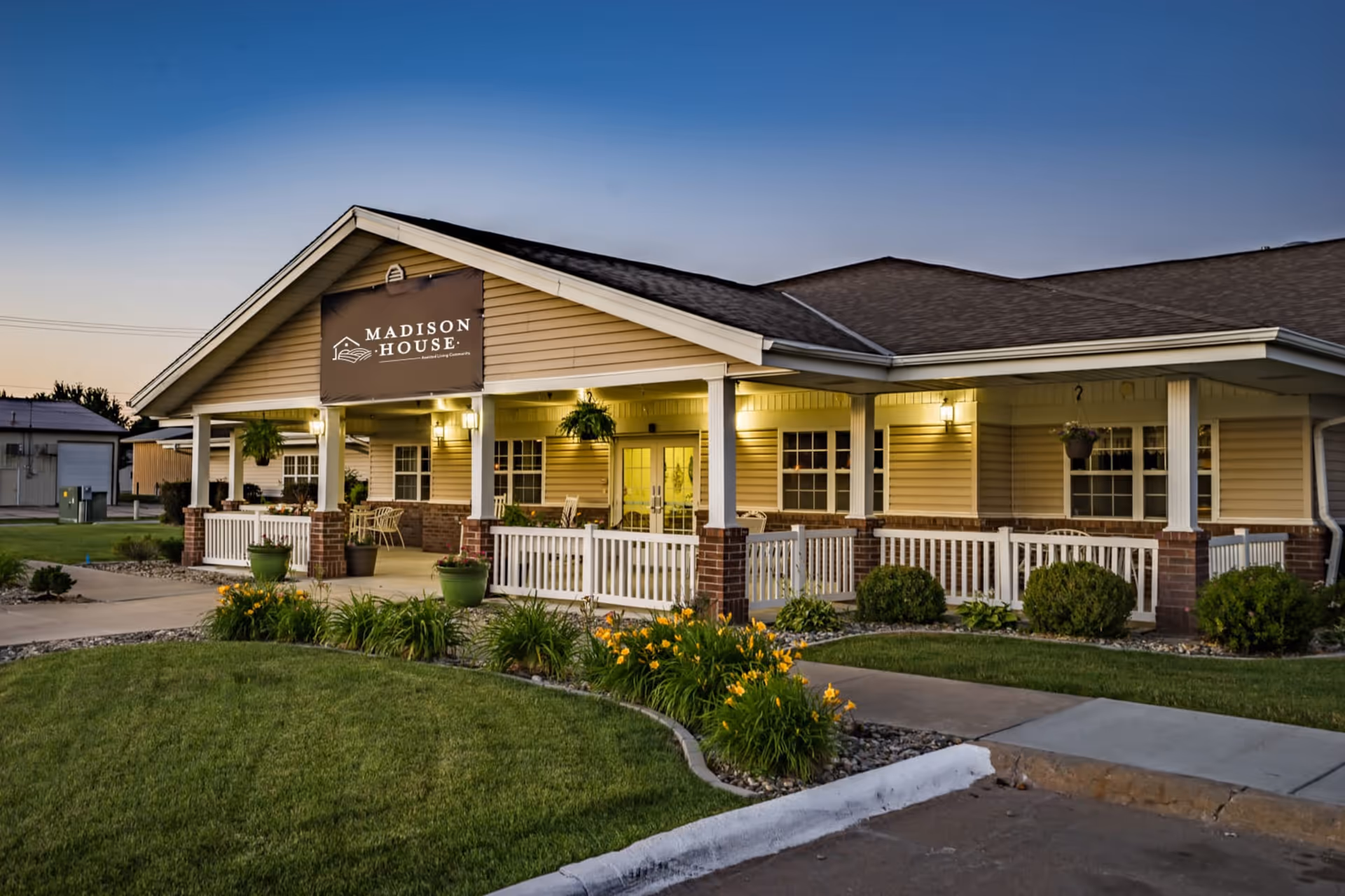 Exterior front view of the Madison House building with a covered porch, lit entrance, and landscaped lawn at dusk.
