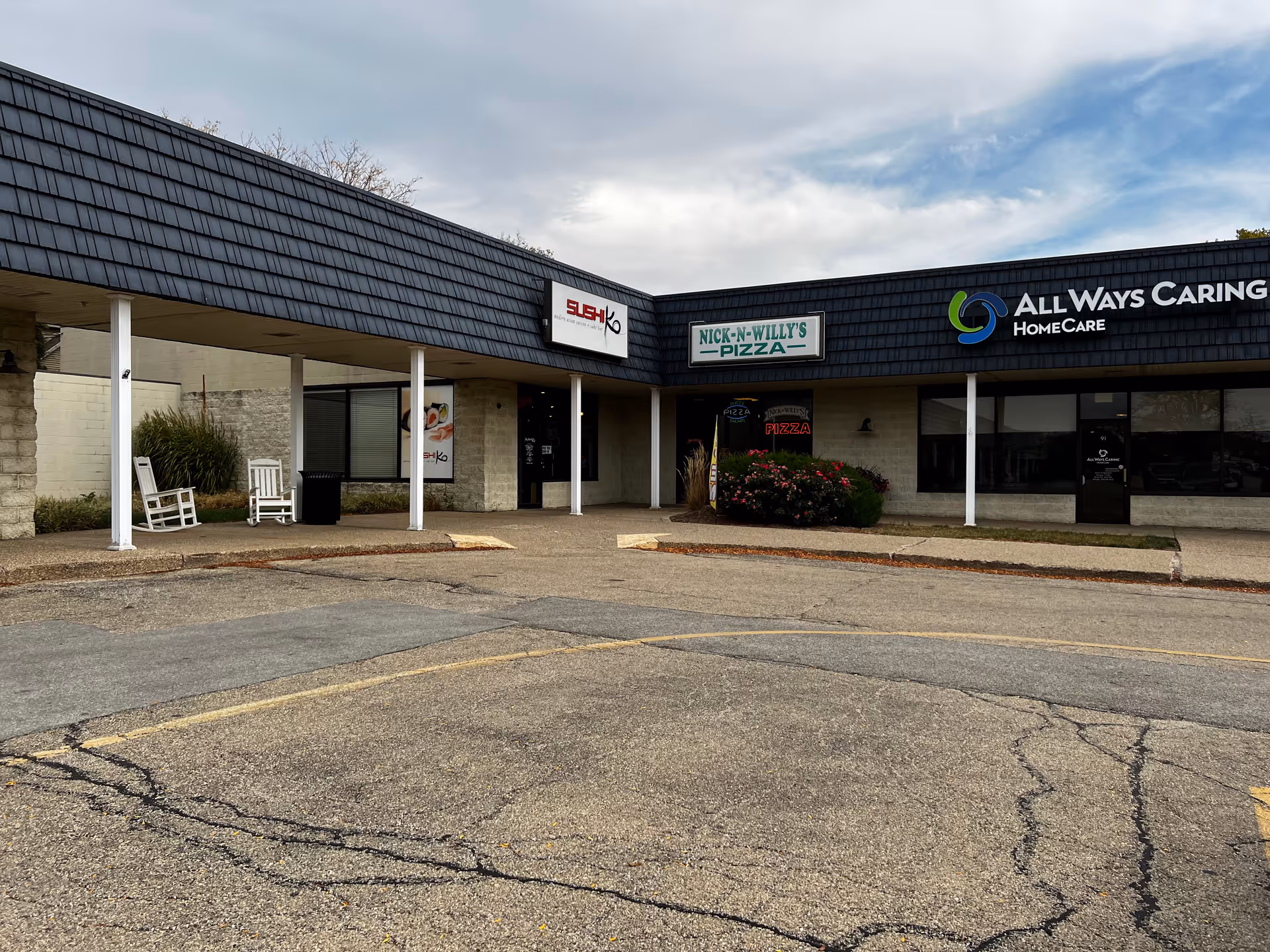 Exterior of a strip mall with All Ways Caring HomeCare sign and neighboring shops.