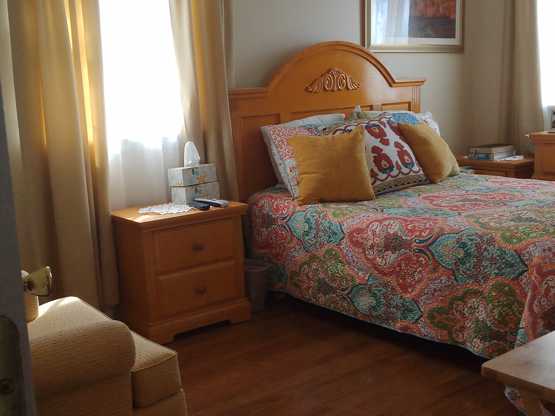 A neatly made bedroom with a colorful quilt, wooden headboard, and two bedside tables.