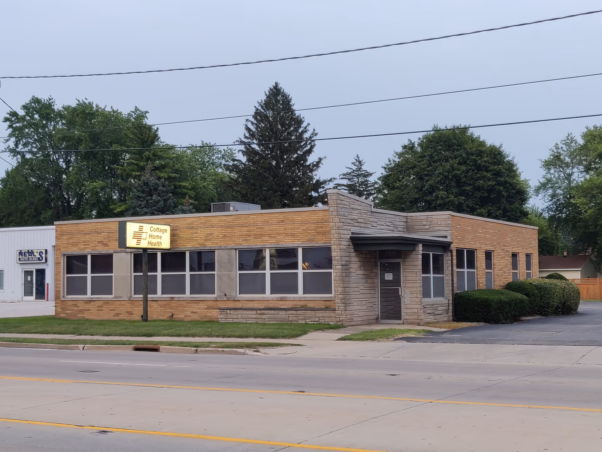 Single-story brick building with Cottage Home Health sign on the front, large windows, and trees