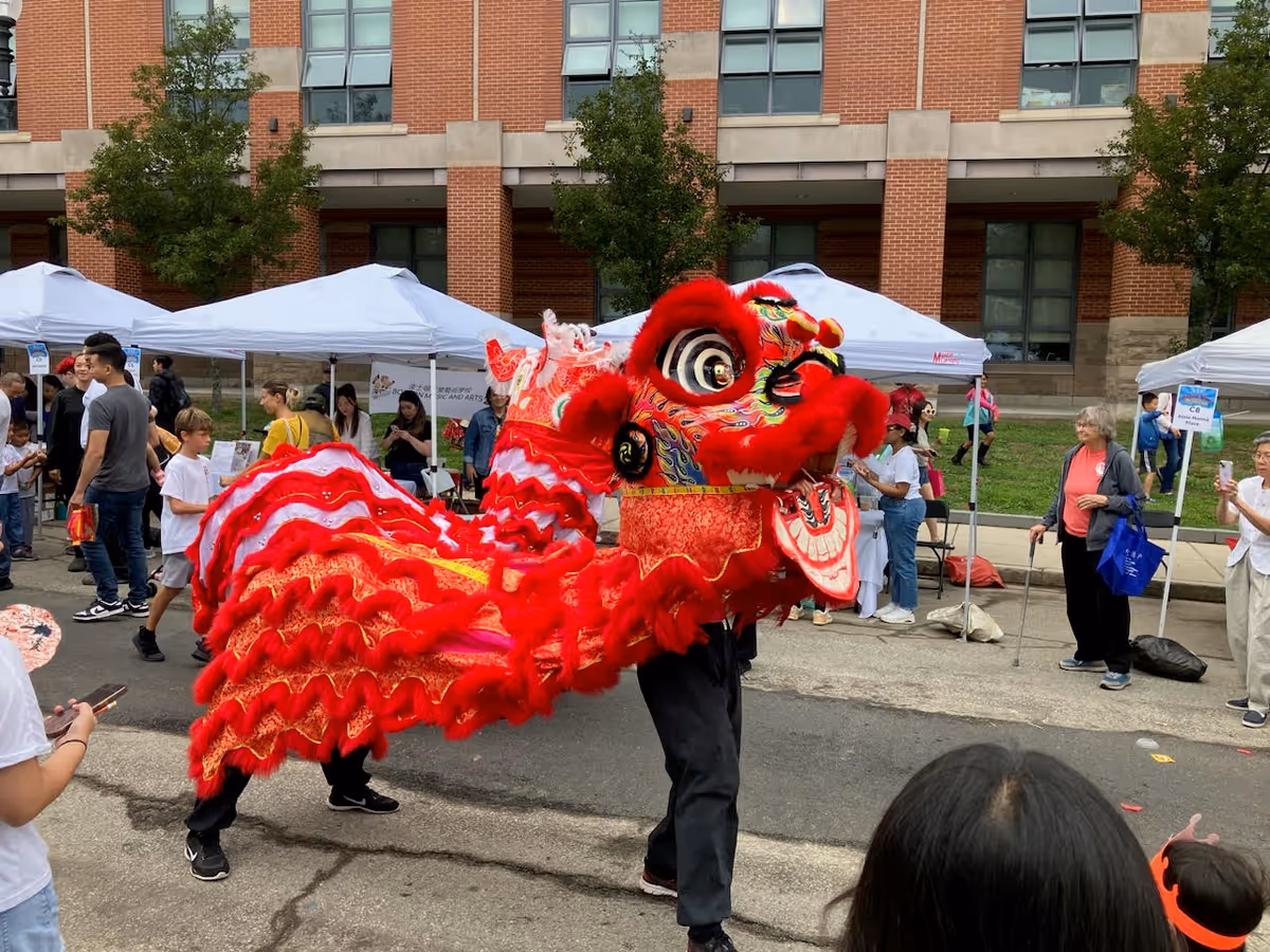 Red dragon dance performing outdoors on a street beside white tents and spectators.