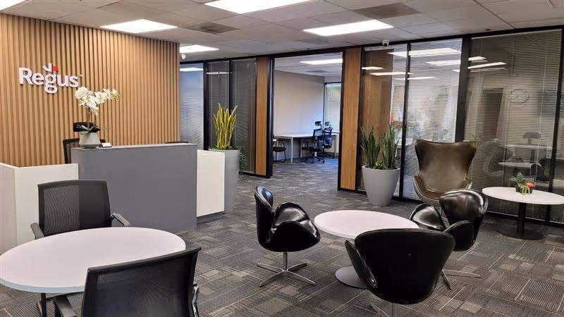 Modern facility lobby with round tables, black chairs, potted plants, and a reception desk.