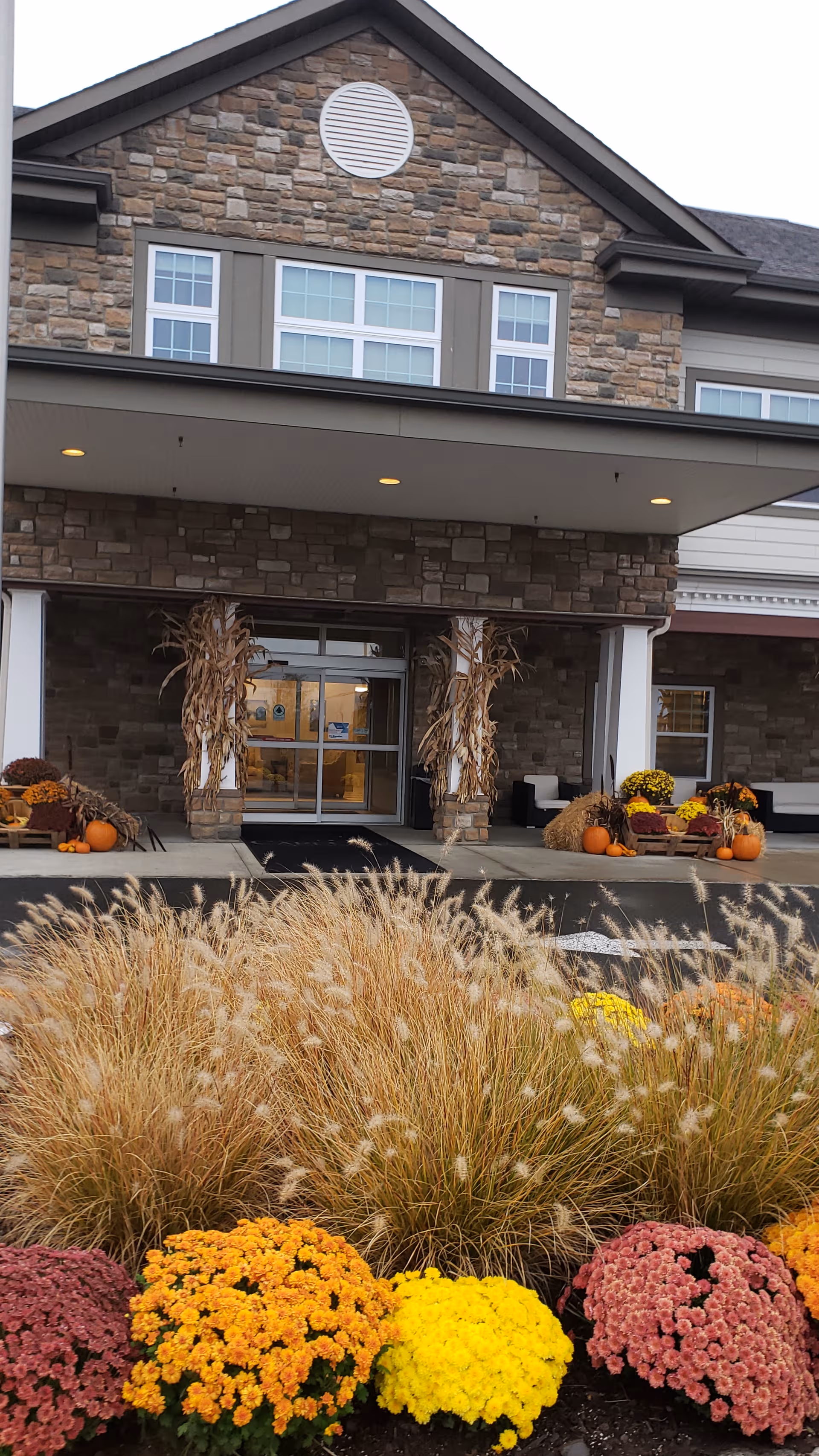 Front entrance of a senior living facility with pumpkins and autumn flowers.