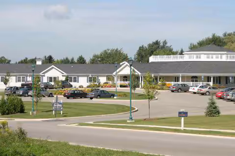 Front exterior view of a single-story senior living building with an entrance canopy, parking lot, and landscaped lawn.