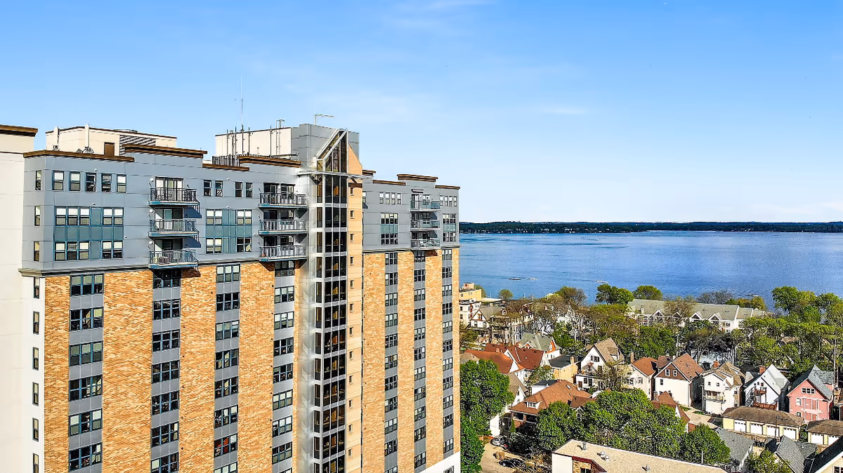 High-rise residential building with balconies beside a lake and nearby houses