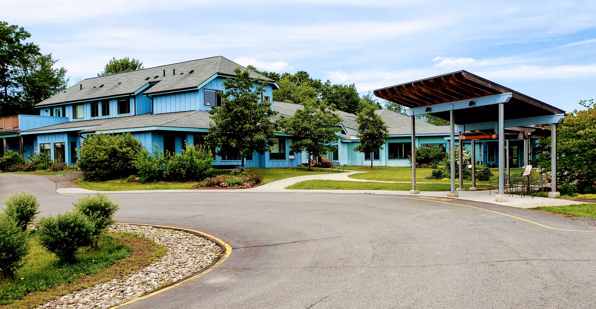 Blue, low-rise senior living facility with curved driveway and covered entrance.