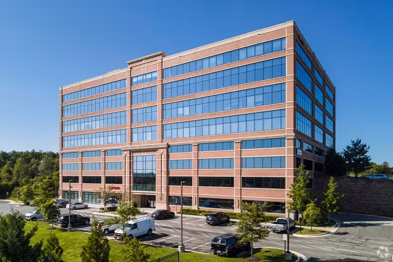 Exterior view of a brick office building with glass windows and a parking lot.