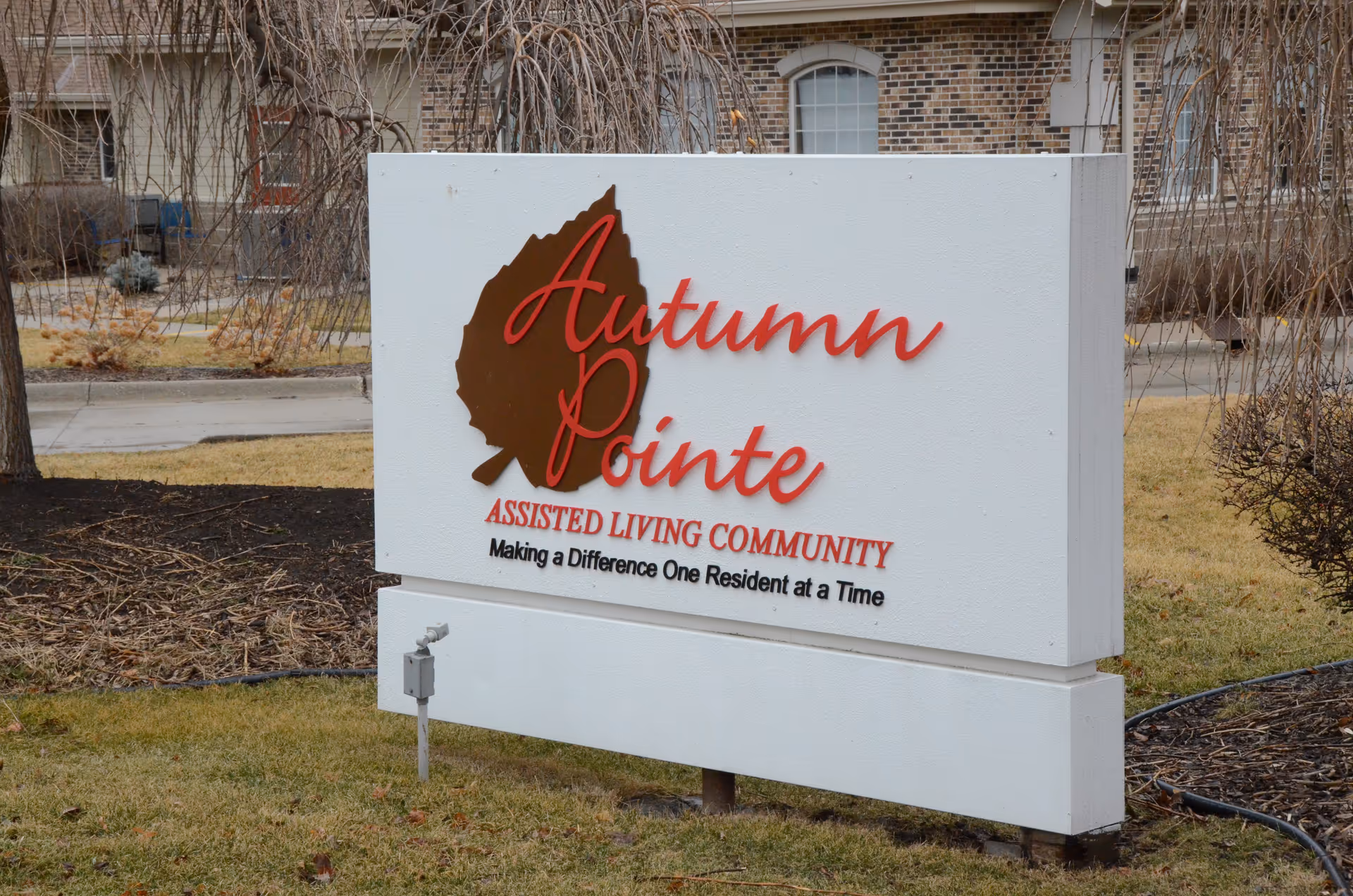 Exterior sign reads Autumn Pointe Assisted Living Community in front of a brick building