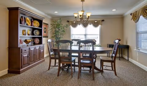 A formal dining room with a wooden table, chairs, a china cabinet, and windows.