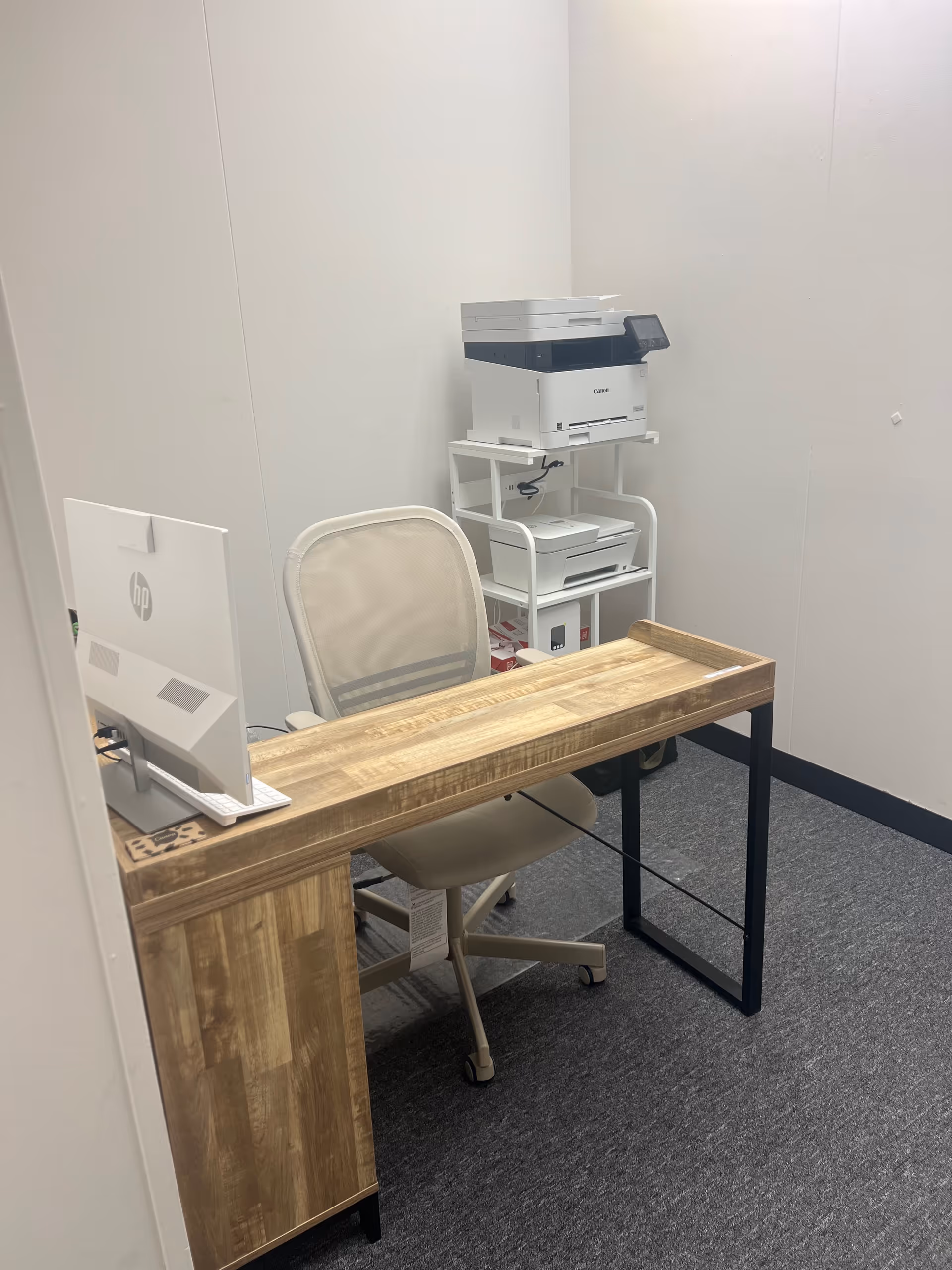 Wooden desk with computer monitor and a stacked printer shelf in a small office.