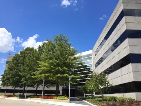 Exterior of a modern senior living facility with glass facade and green trees.