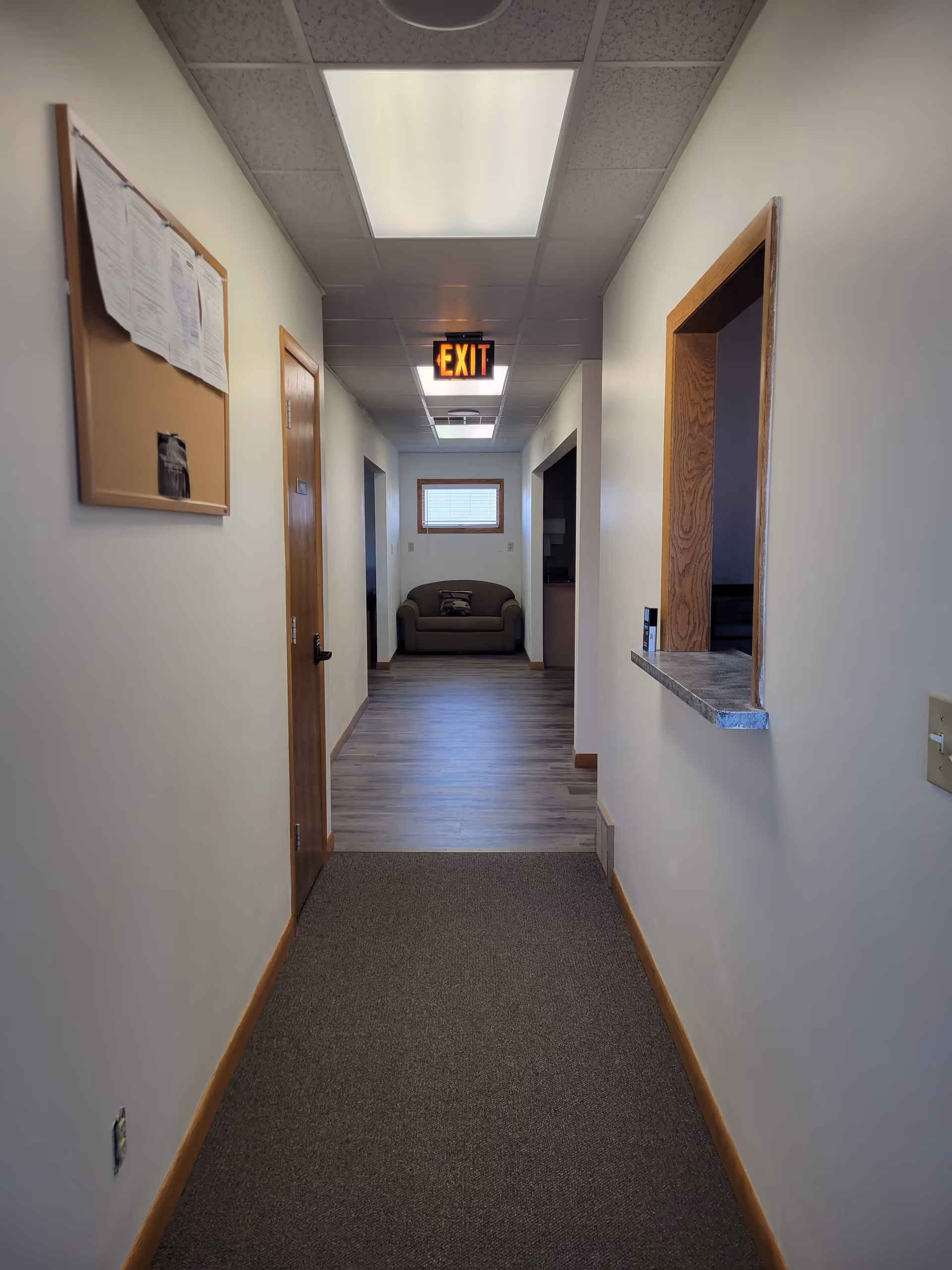 Long hallway inside a senior living facility, with an exit sign and couch at the end.