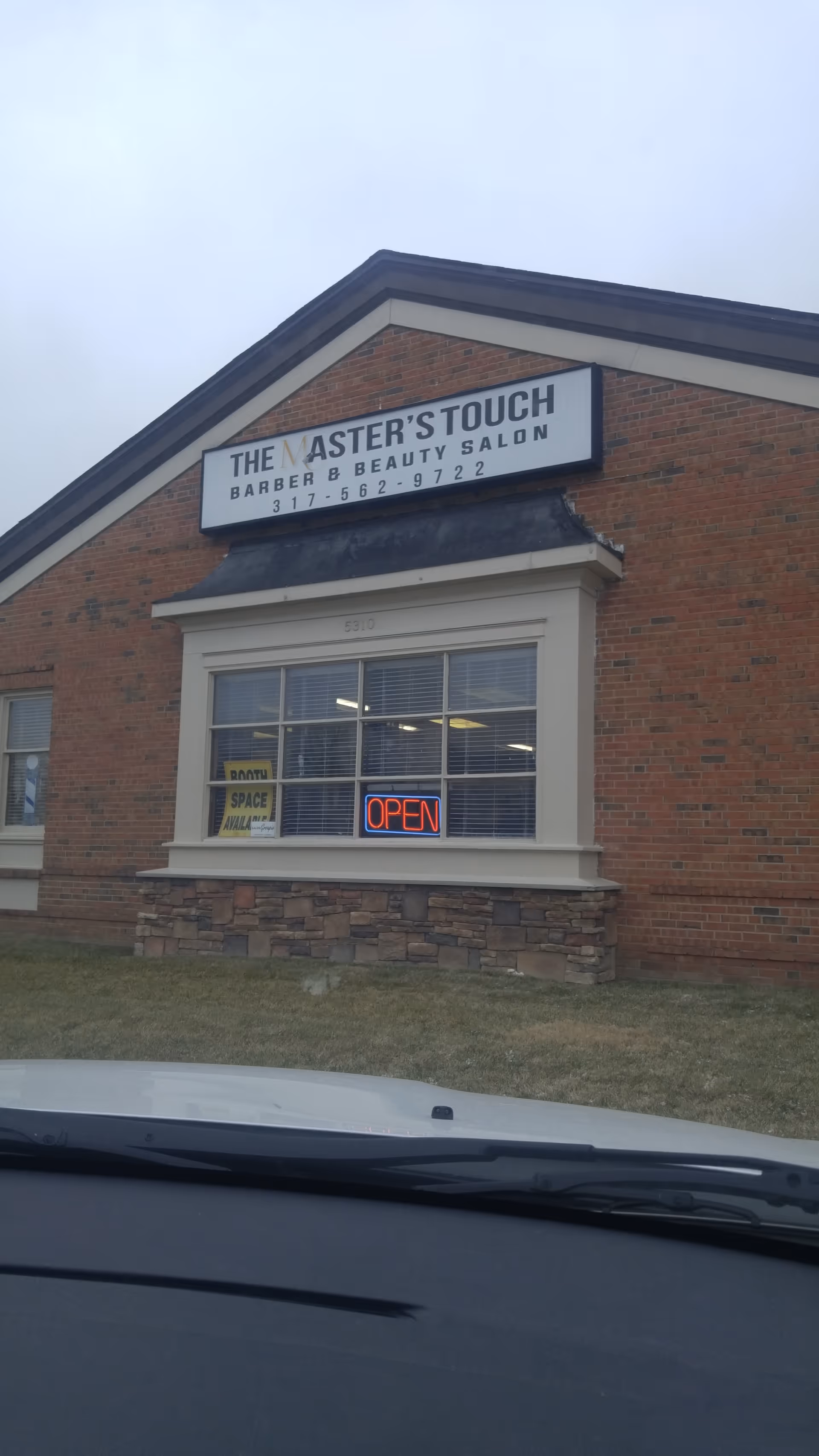 Brick building with The Master's Touch Barber & Beauty Salon sign and open neon window.