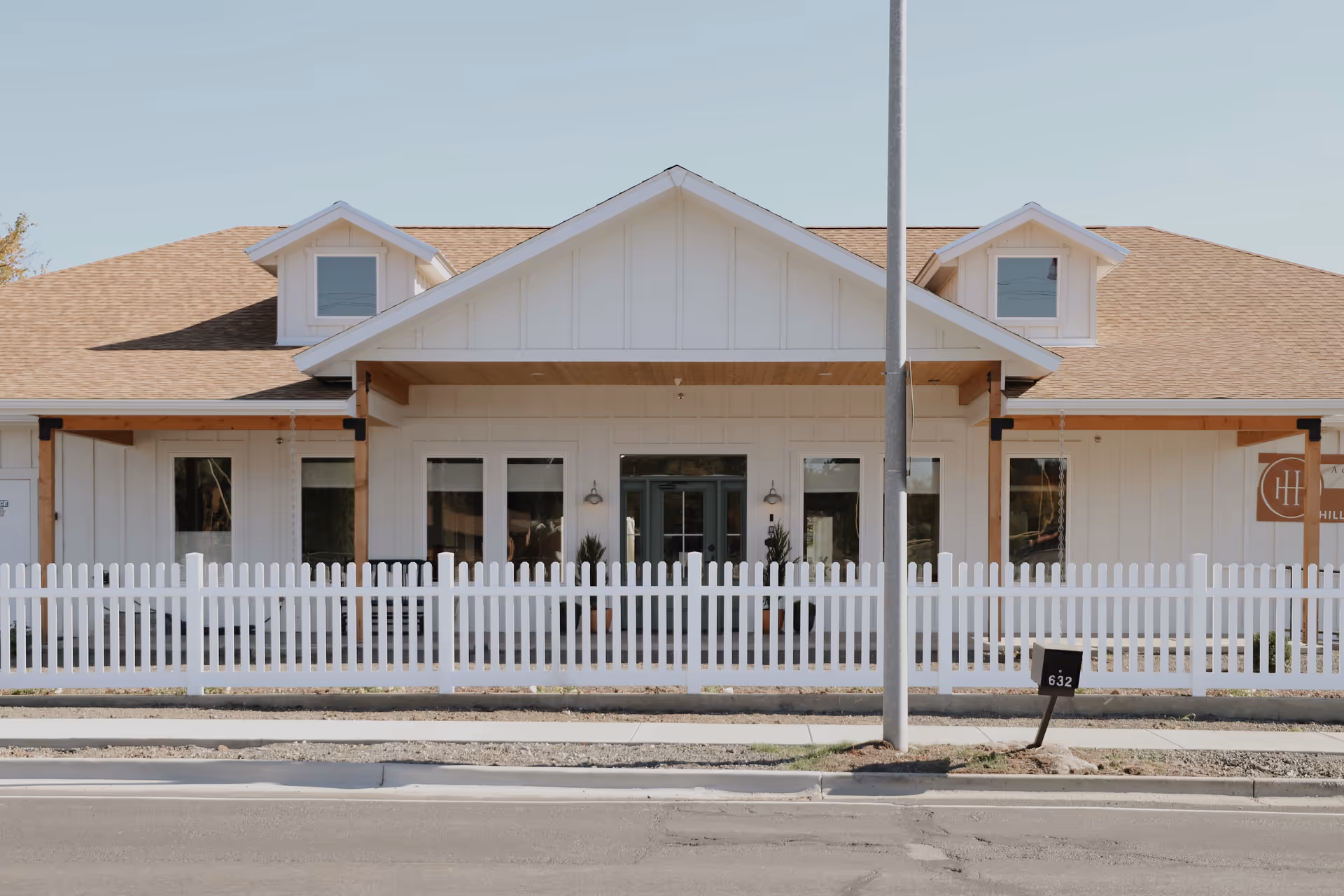 Front view of Hill House Memory Care building with white picket fence along the sidewalk.