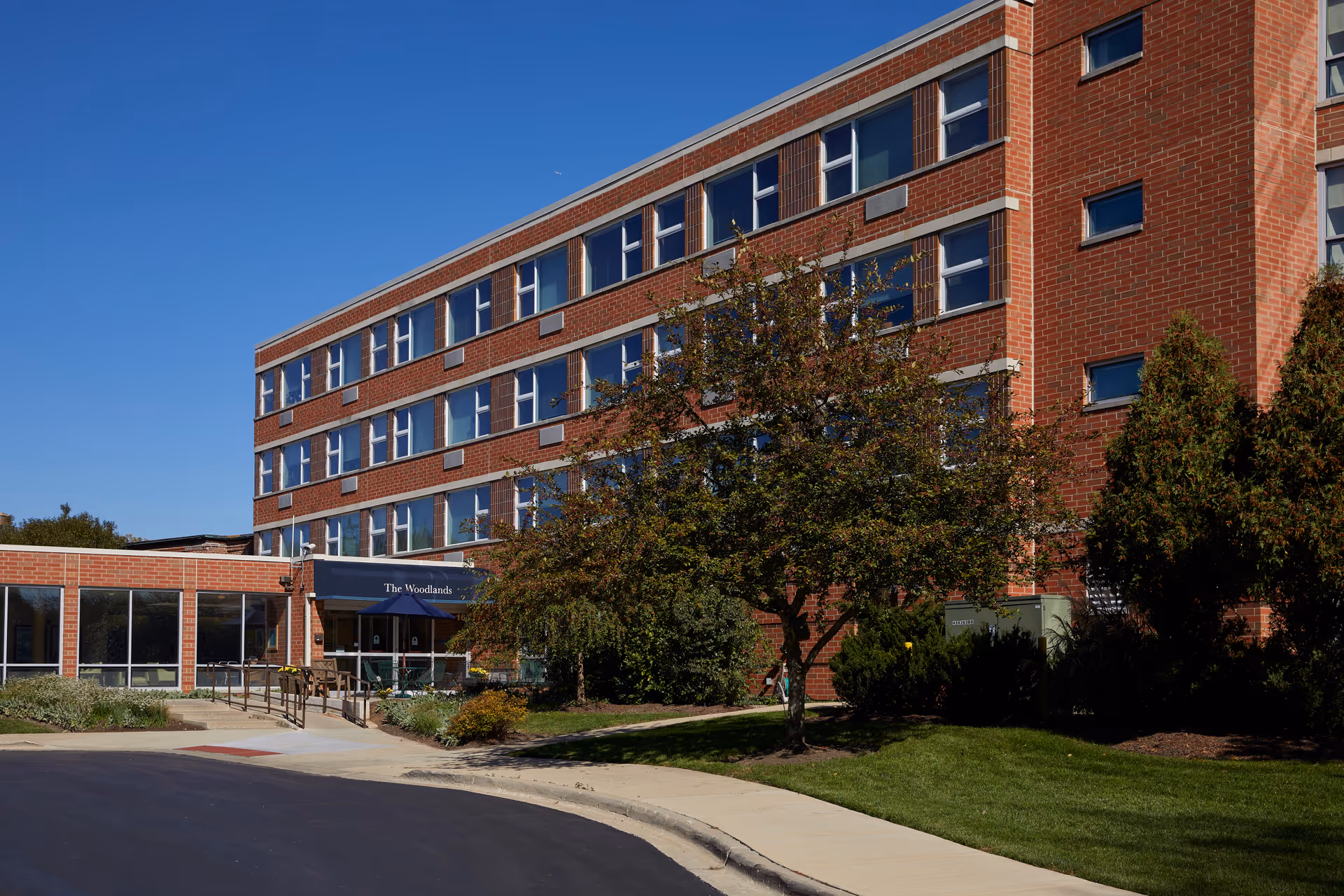Brick senior living facility exterior with entrance, trees, and a blue sky.