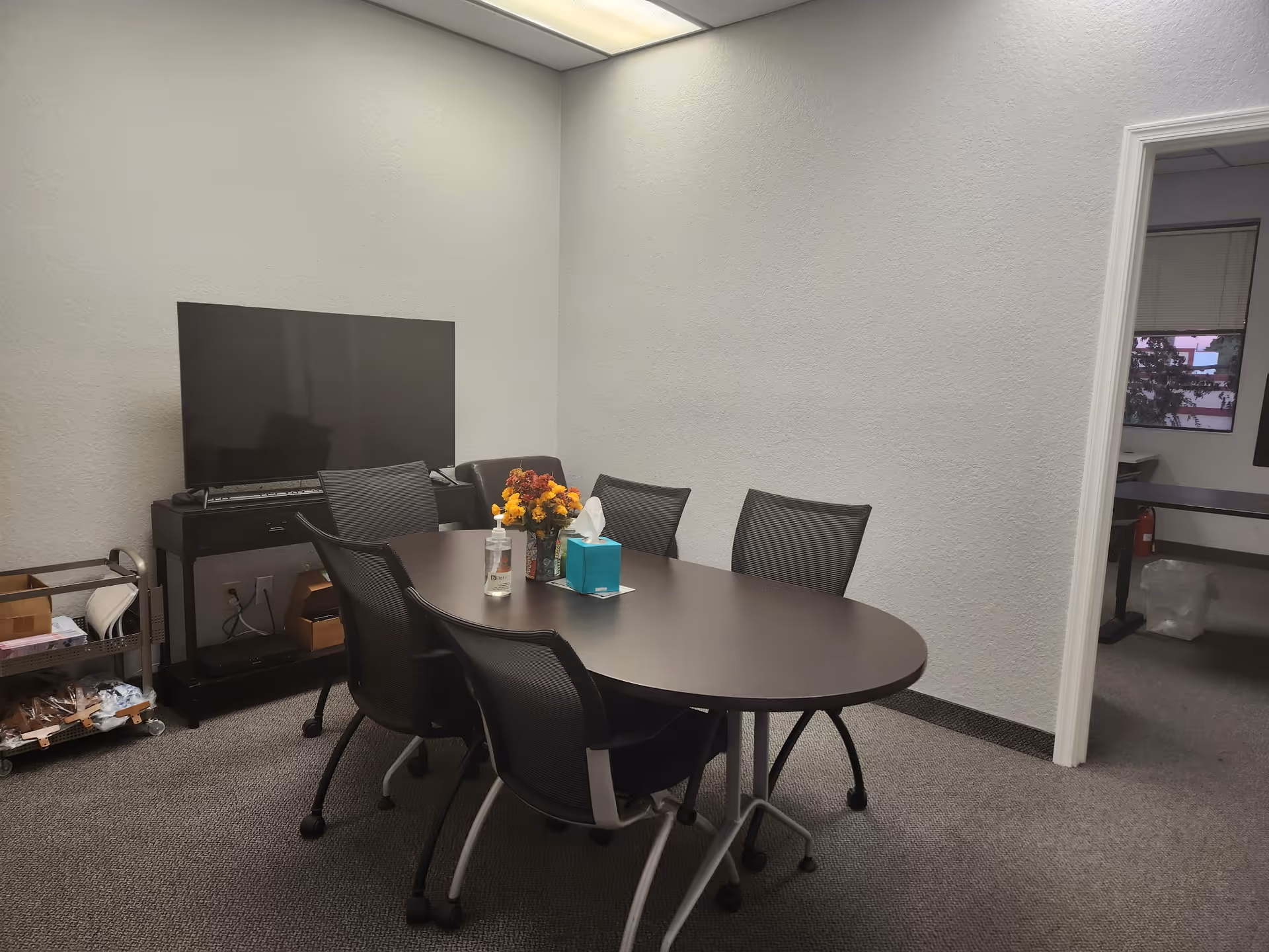 A small conference room with a round table, chairs, TV, and a cart.