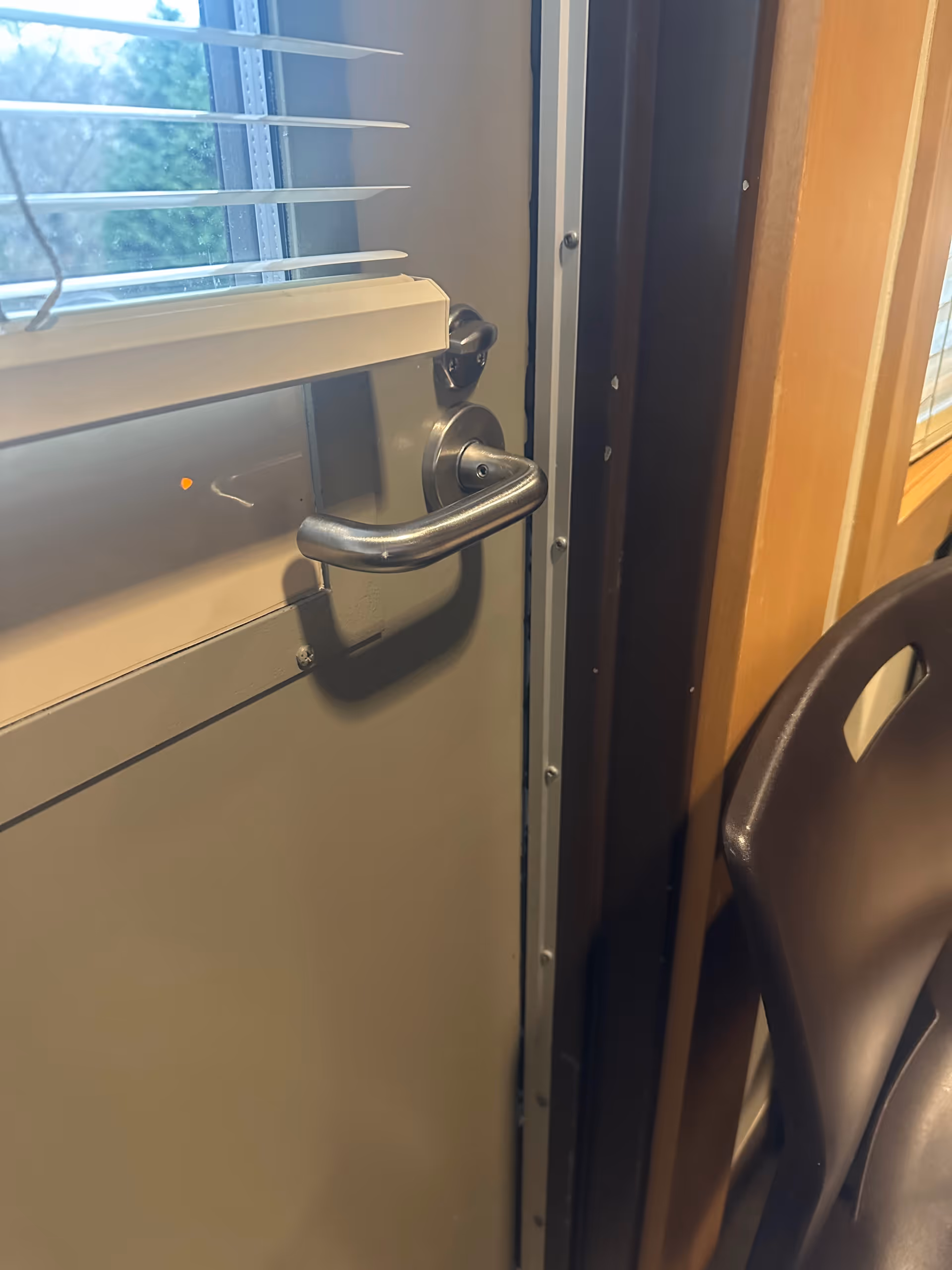 Interior door with metal handle beside a window and chair.