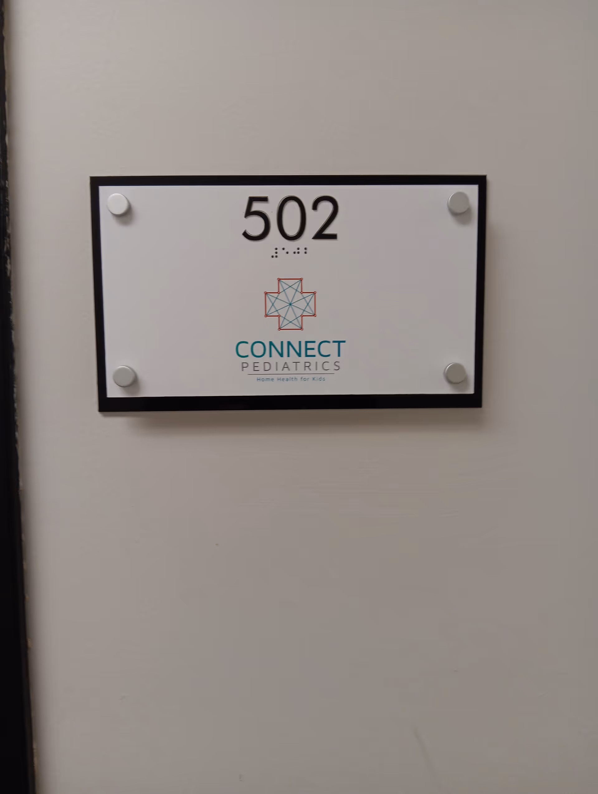 Wall-mounted room sign reading 502 with Connect Pediatrics logo on a beige wall.