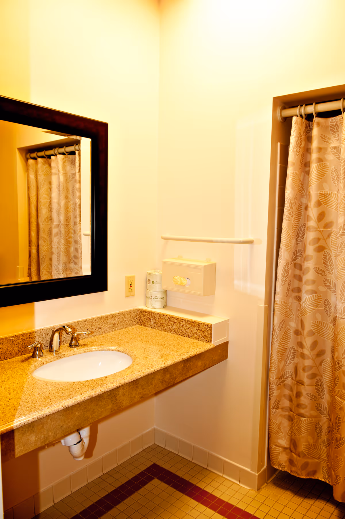 Senior living bathroom with sink, mirror, towel rack, and patterned shower curtain.